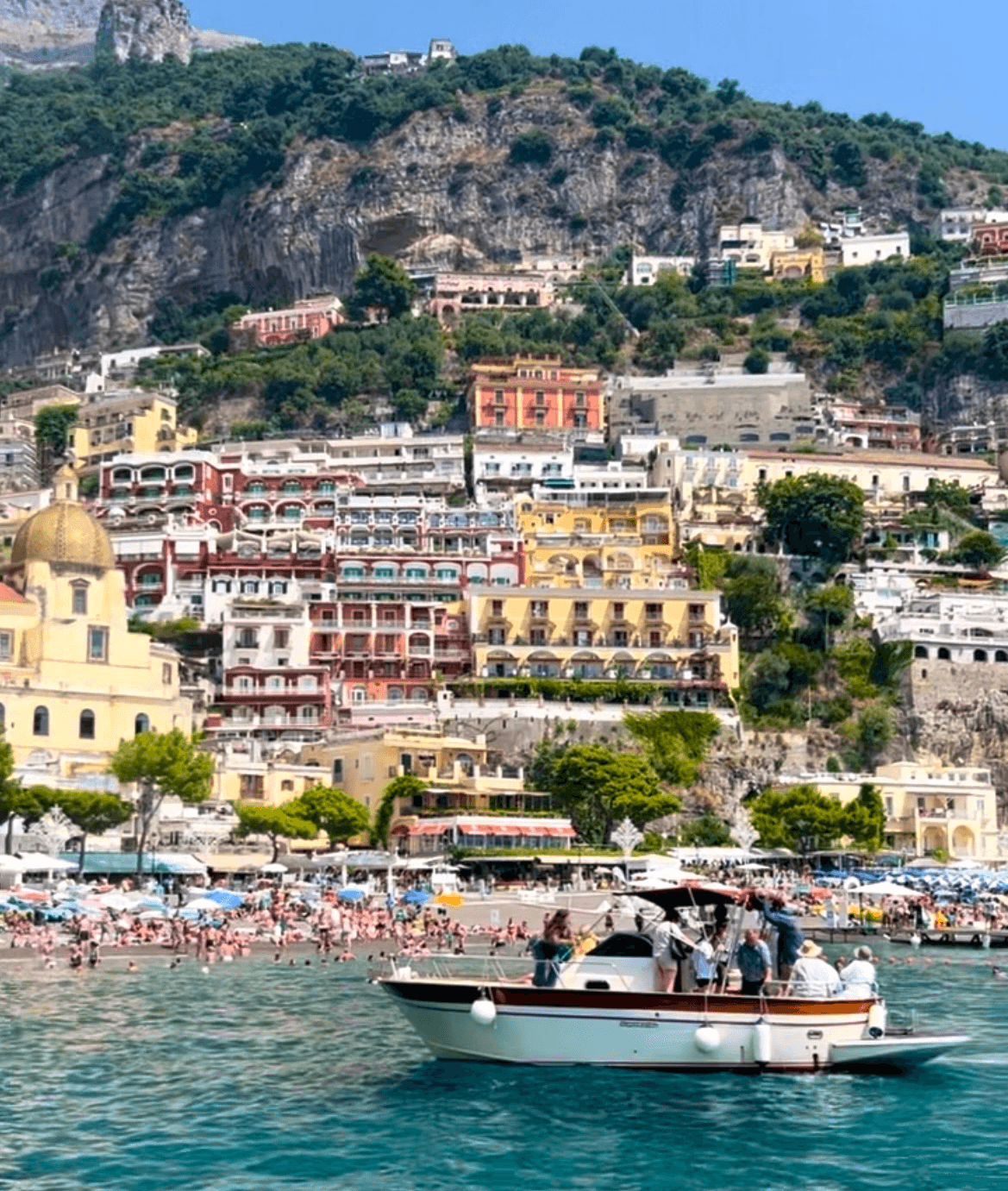 A boat full of people in the water in front of a busy coastline