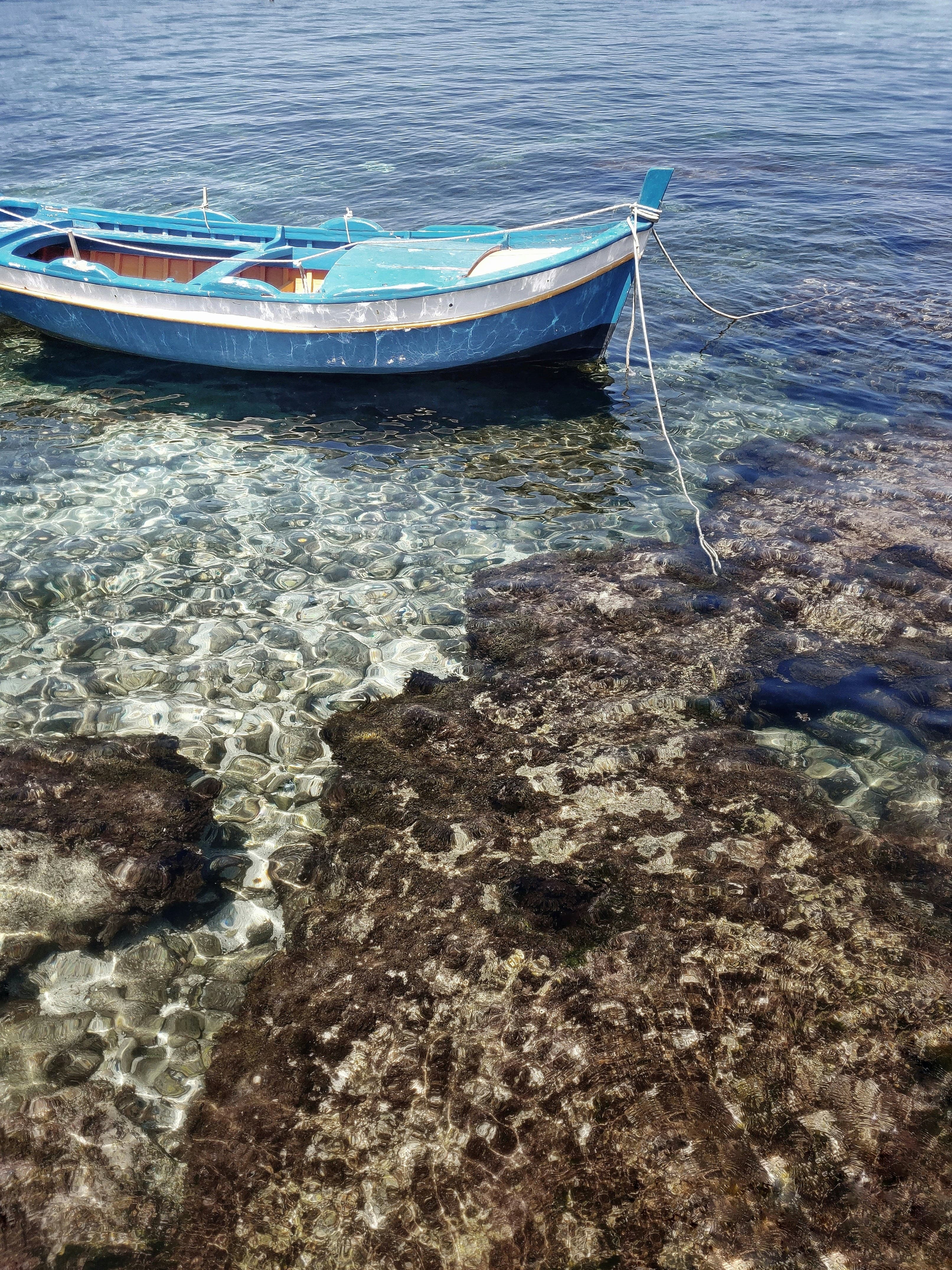 A small fishing boat drifting in the beautiful crystal clear water off the shore with rocks.