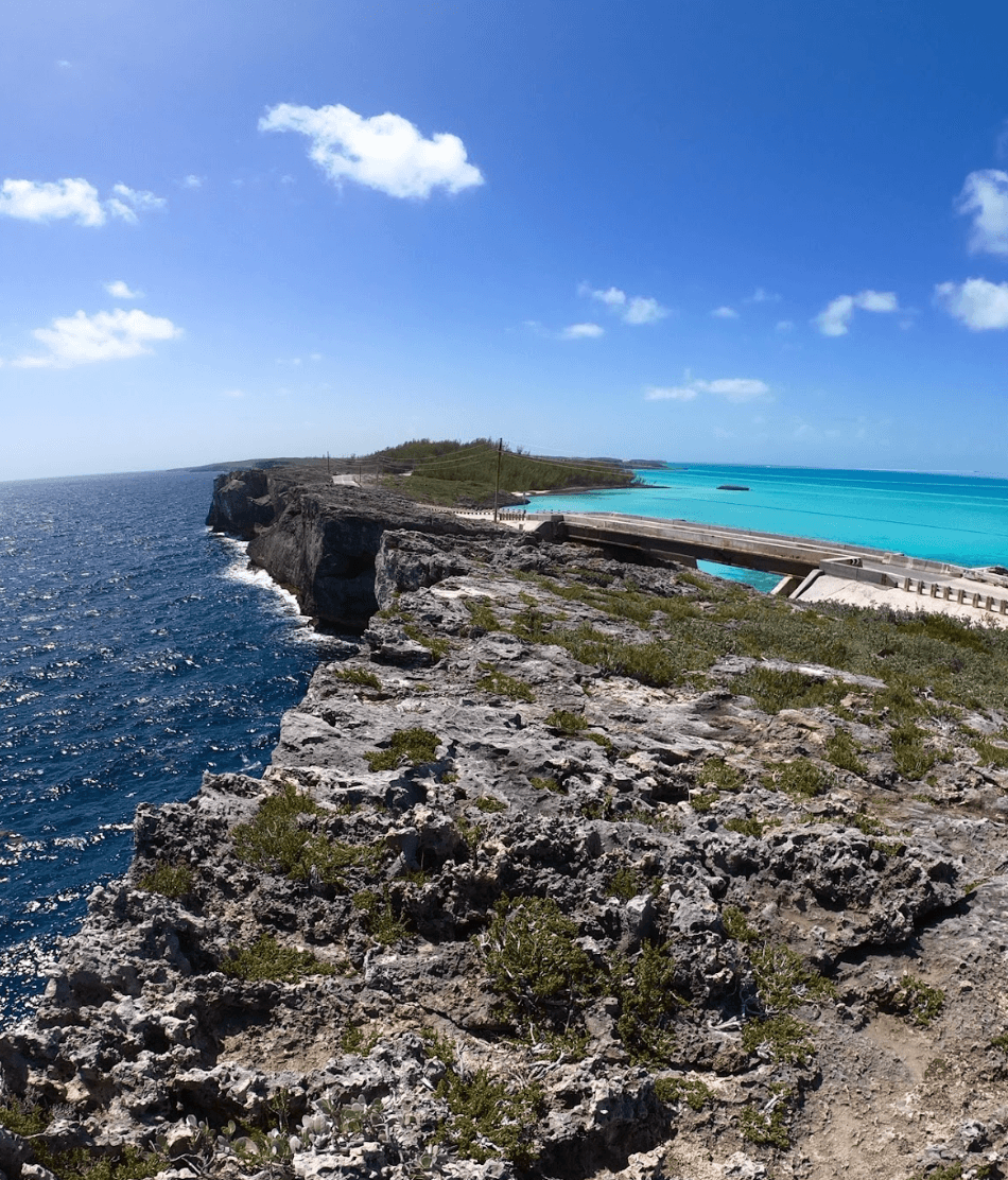 A view of blue water near a rocky shoreline and bridge during the daytime.
