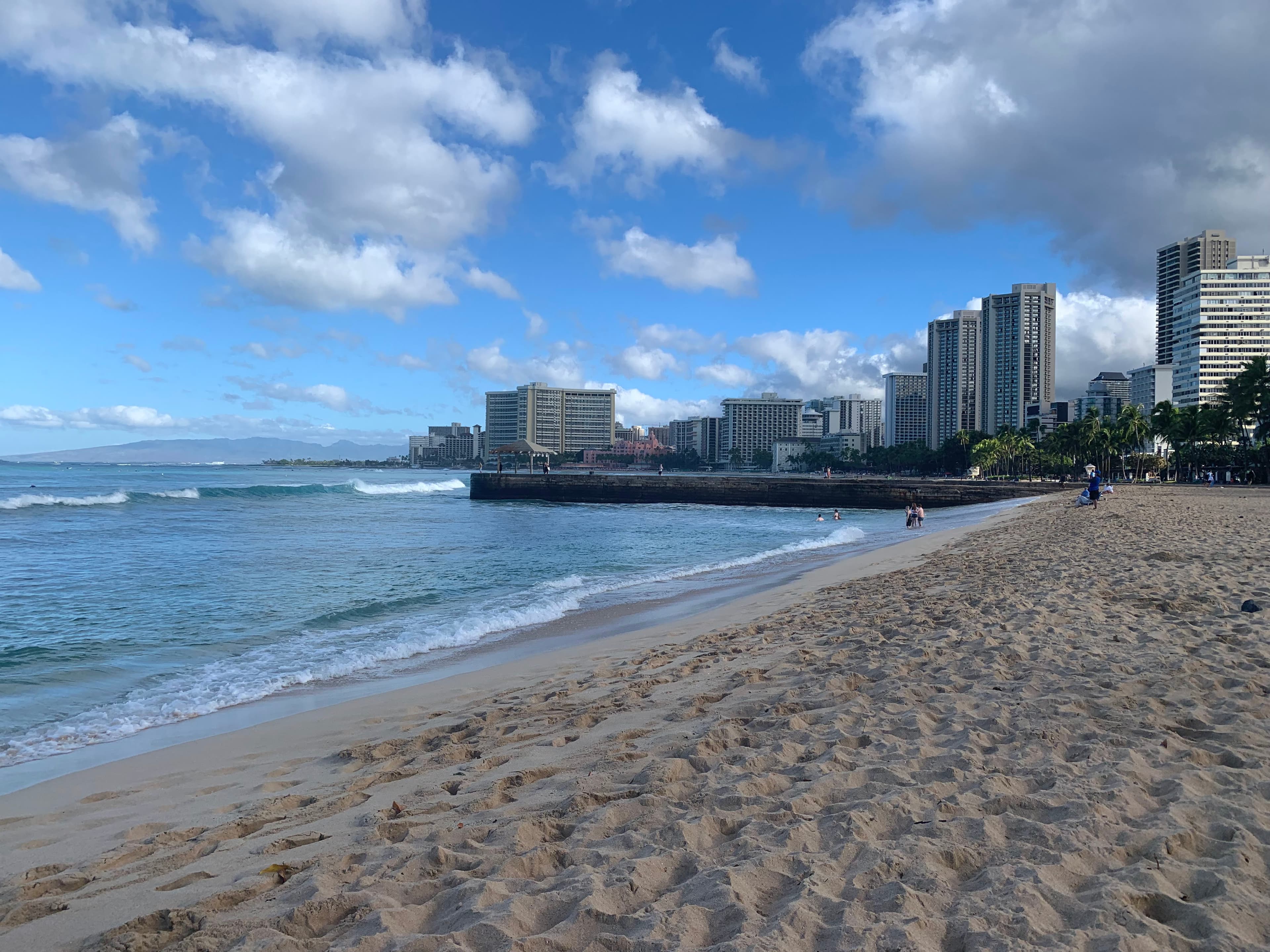 A view of a sandy beach with a city skyline along the coast in the background.