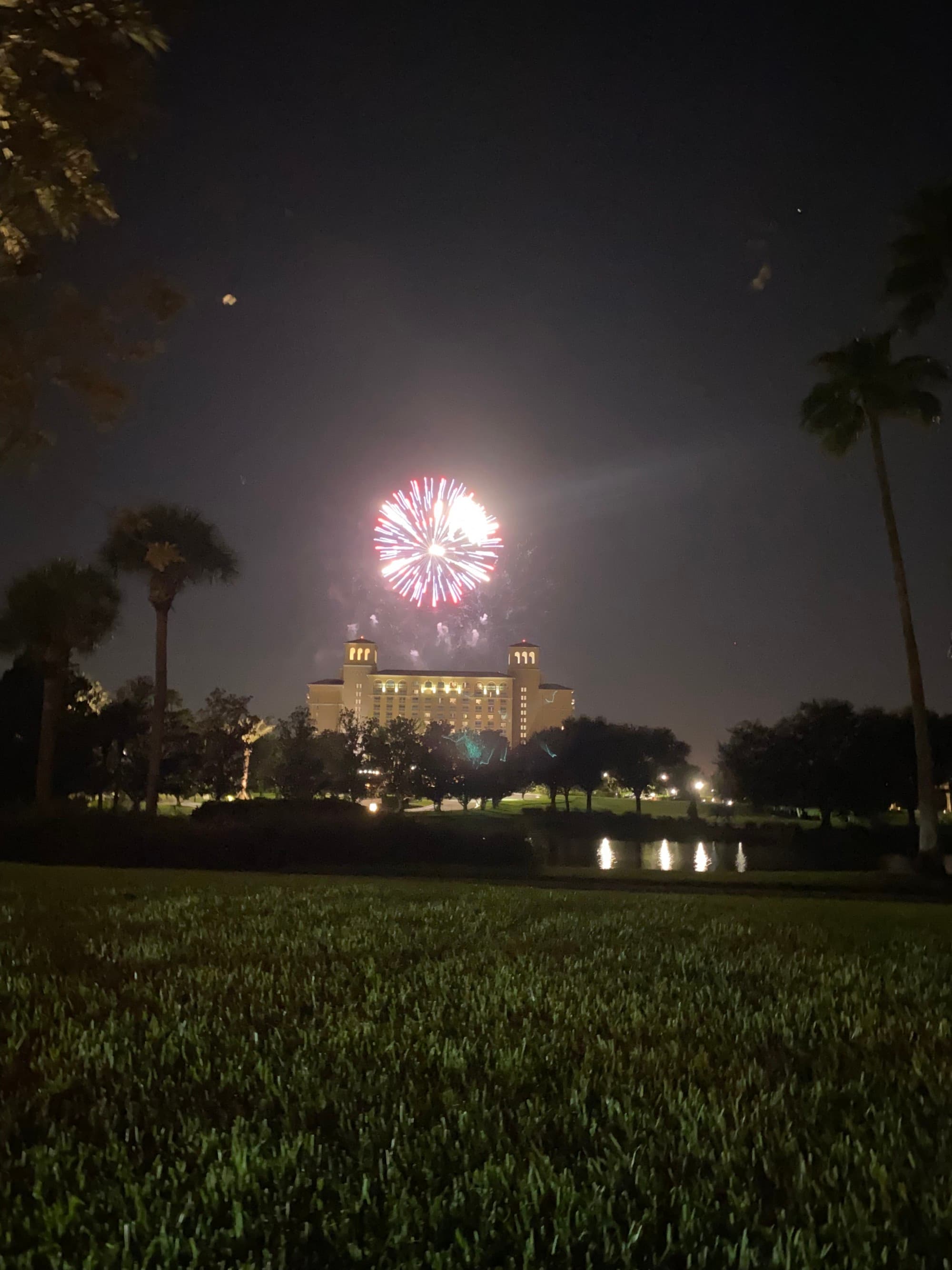 A picture taken from a far of fireworks at night above a building.
