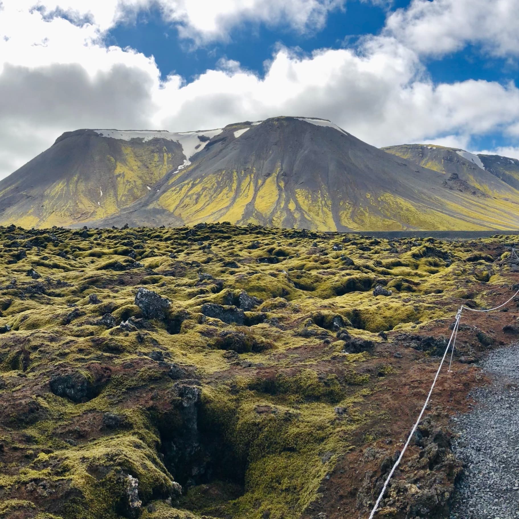Green valley with green mountains and partially cloudy sky.