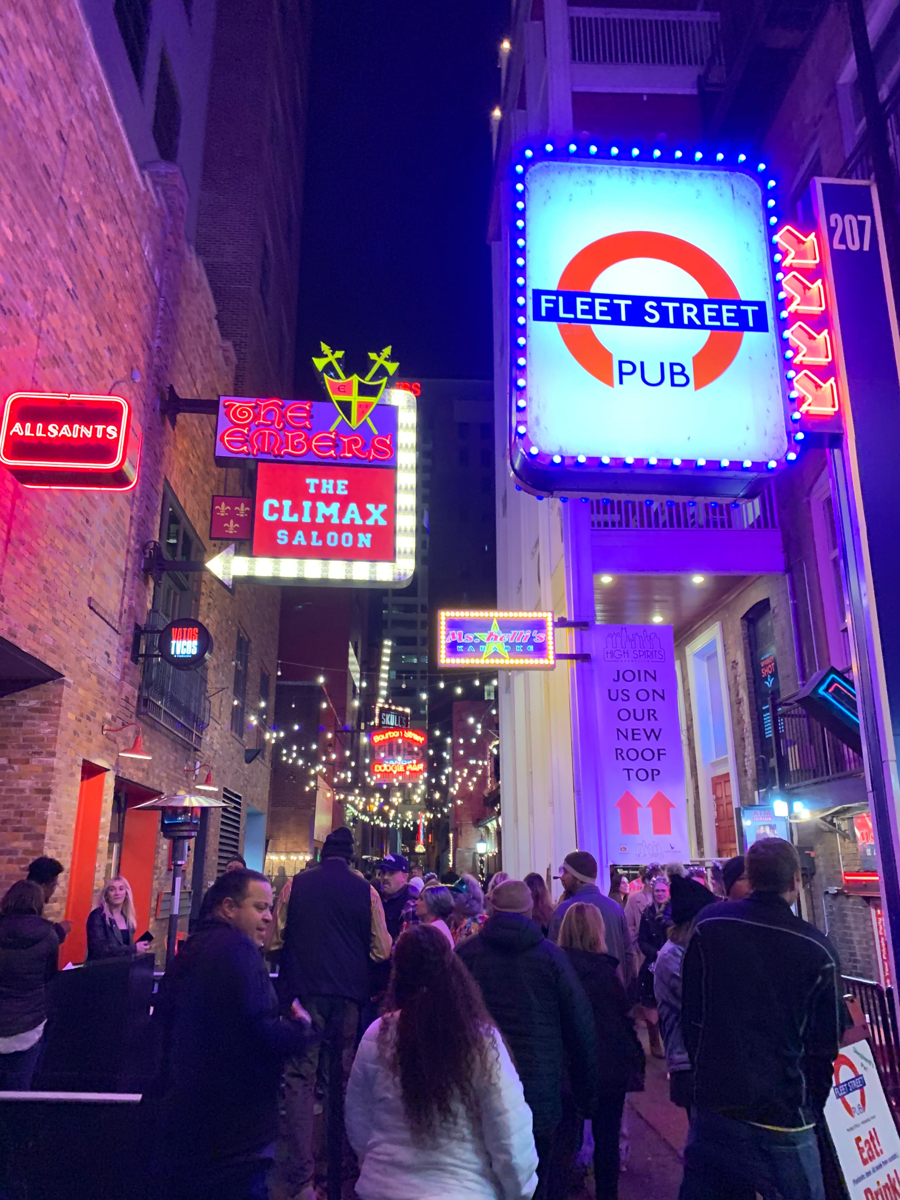 Fleet Street in Nashville at night with neon lights and people walking around outside.
