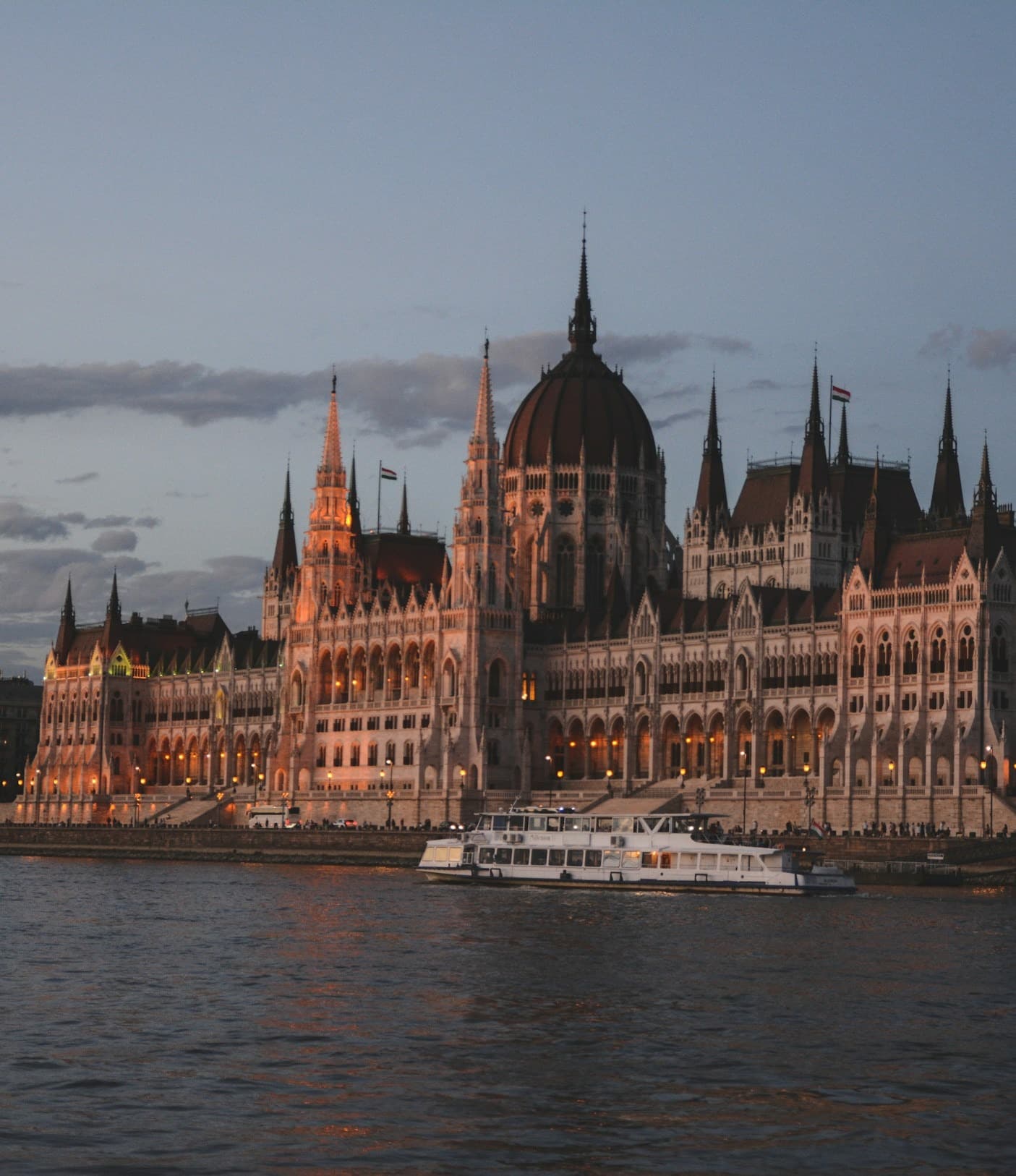 Sunset cruise at Danube River – a white boat on the river in front of The Parliament House of Hungary.