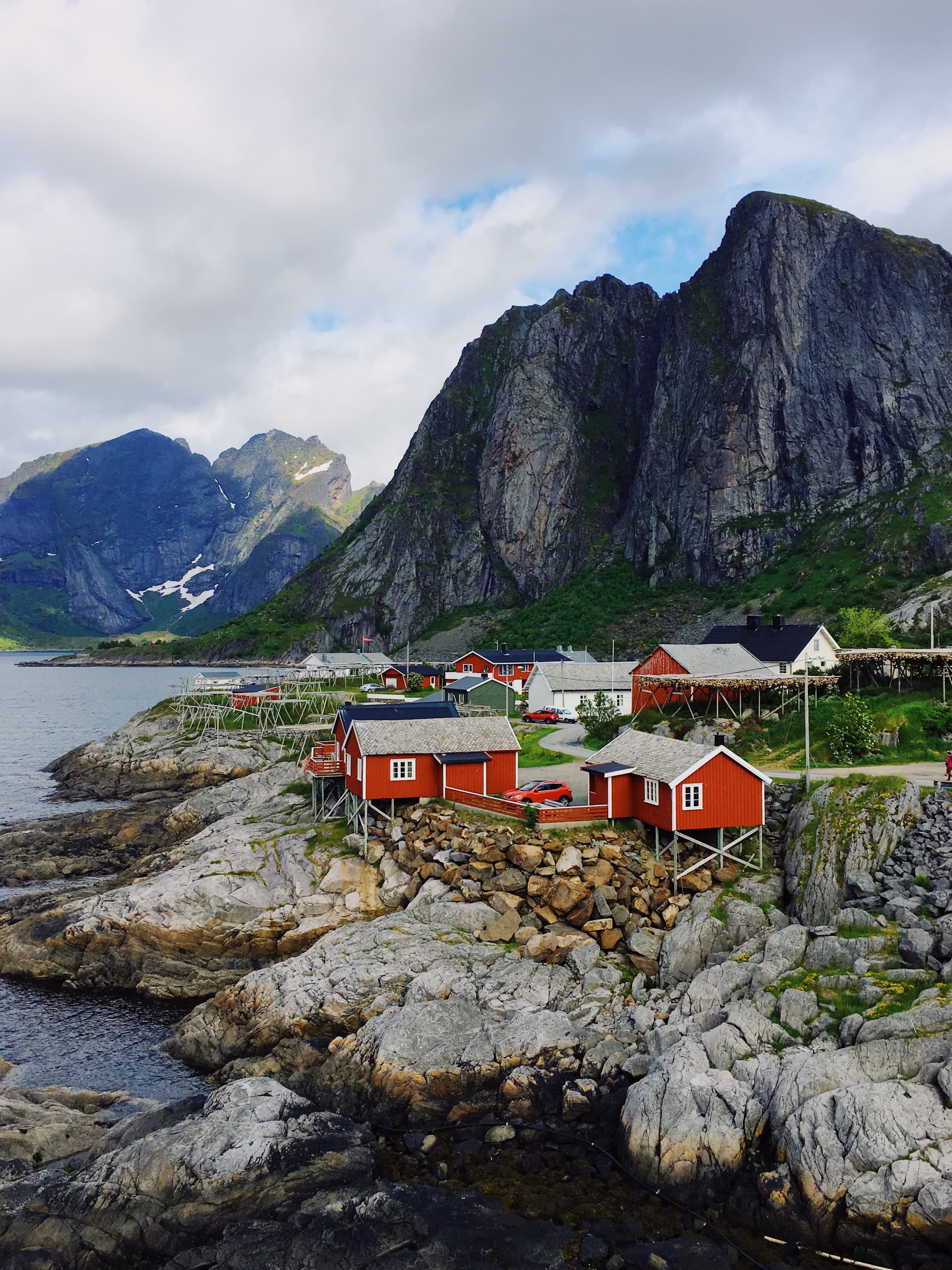 Red houses next to mountain and body of water with cloudy skies during daytime