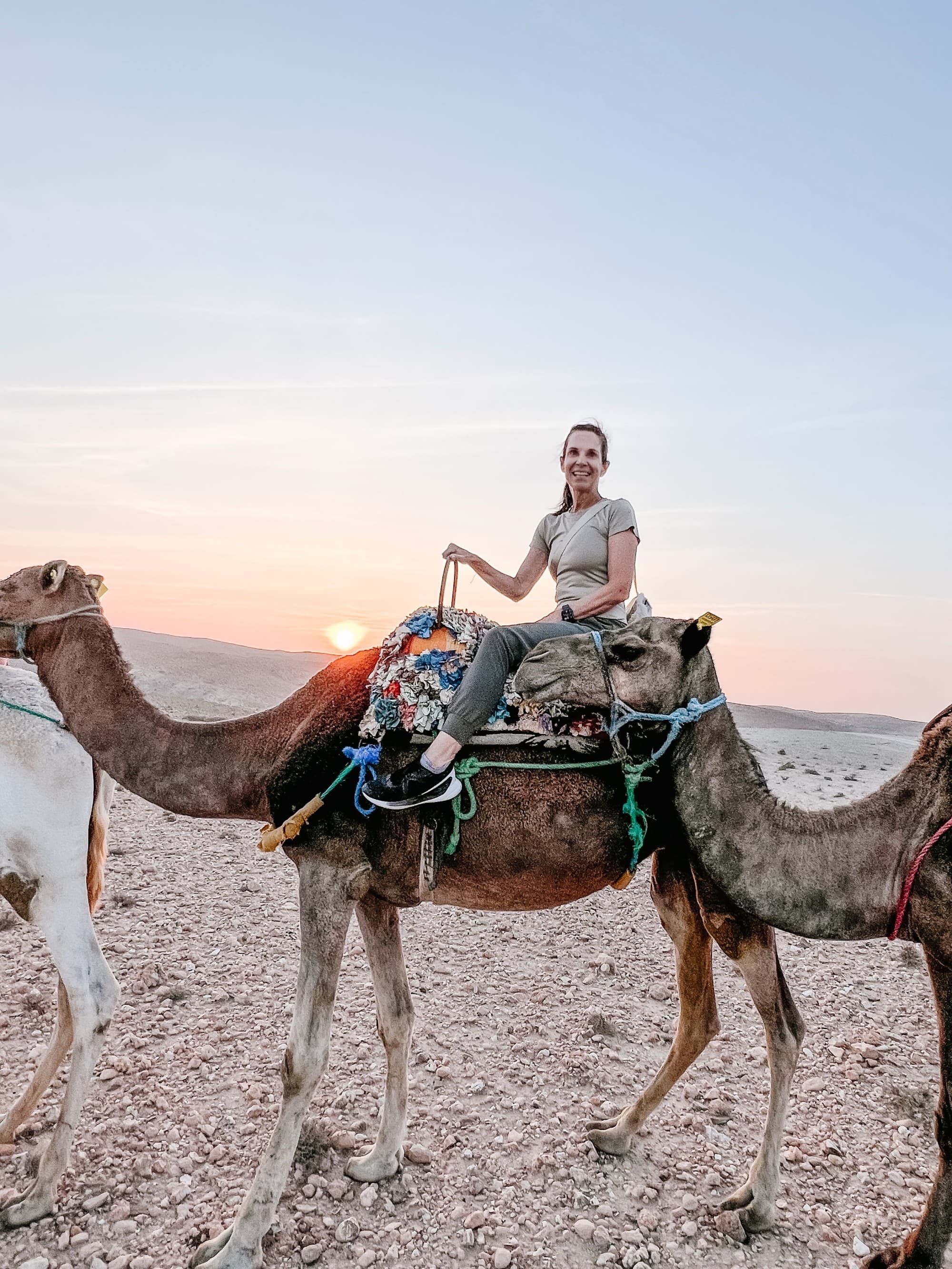 A lady sitting on a camel during sunset.