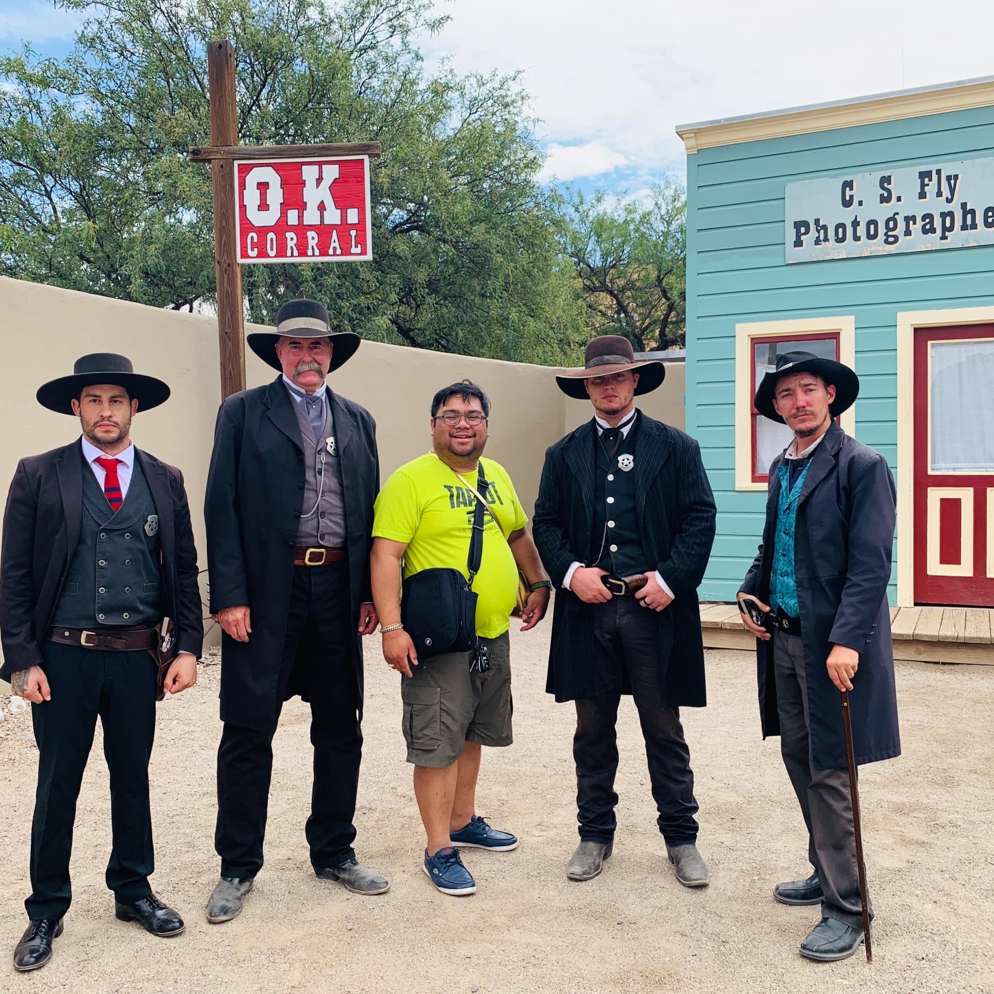 A picture of men posing in black hats and long black coats in front of an old building.