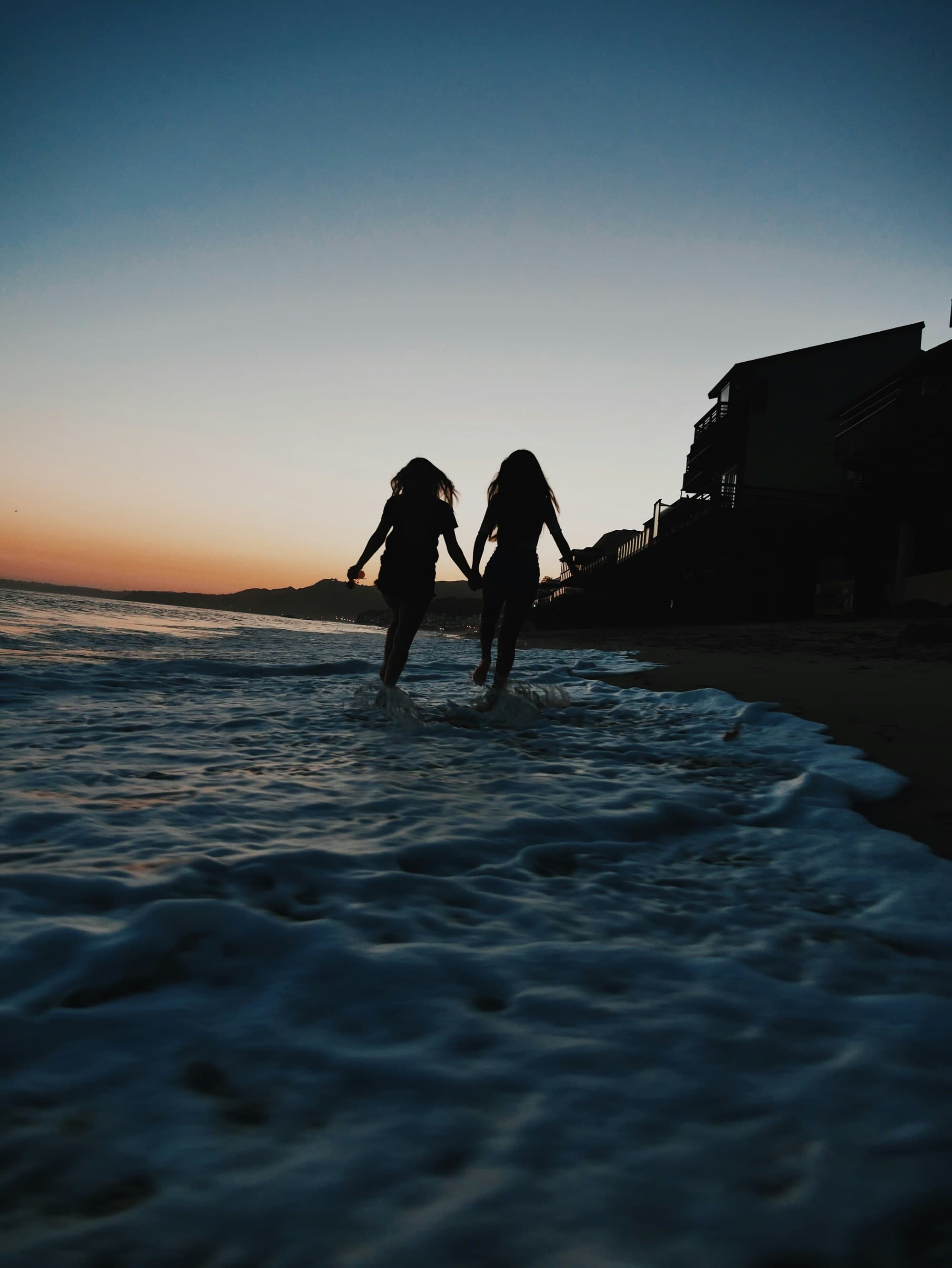 A picture of silhouette of two women running across seashore.