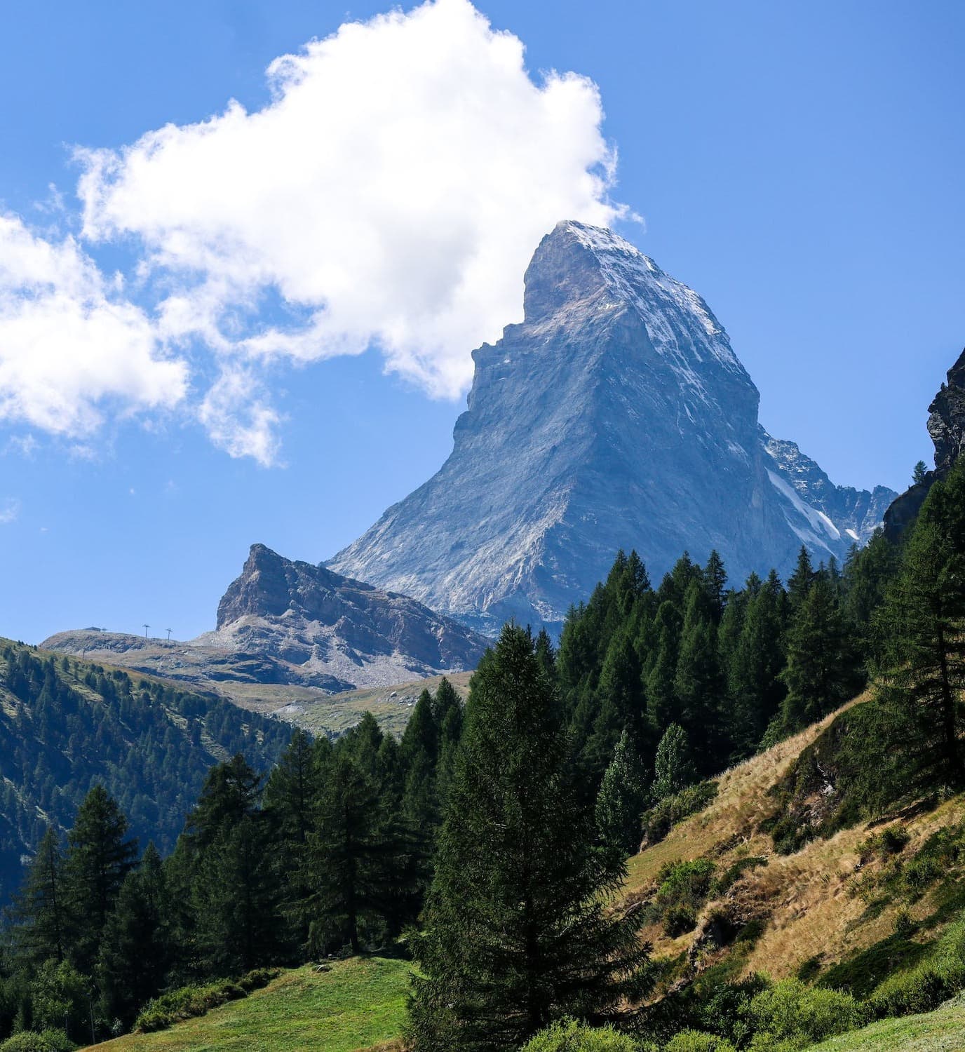 A tall mountain with green trees in front during the daytime