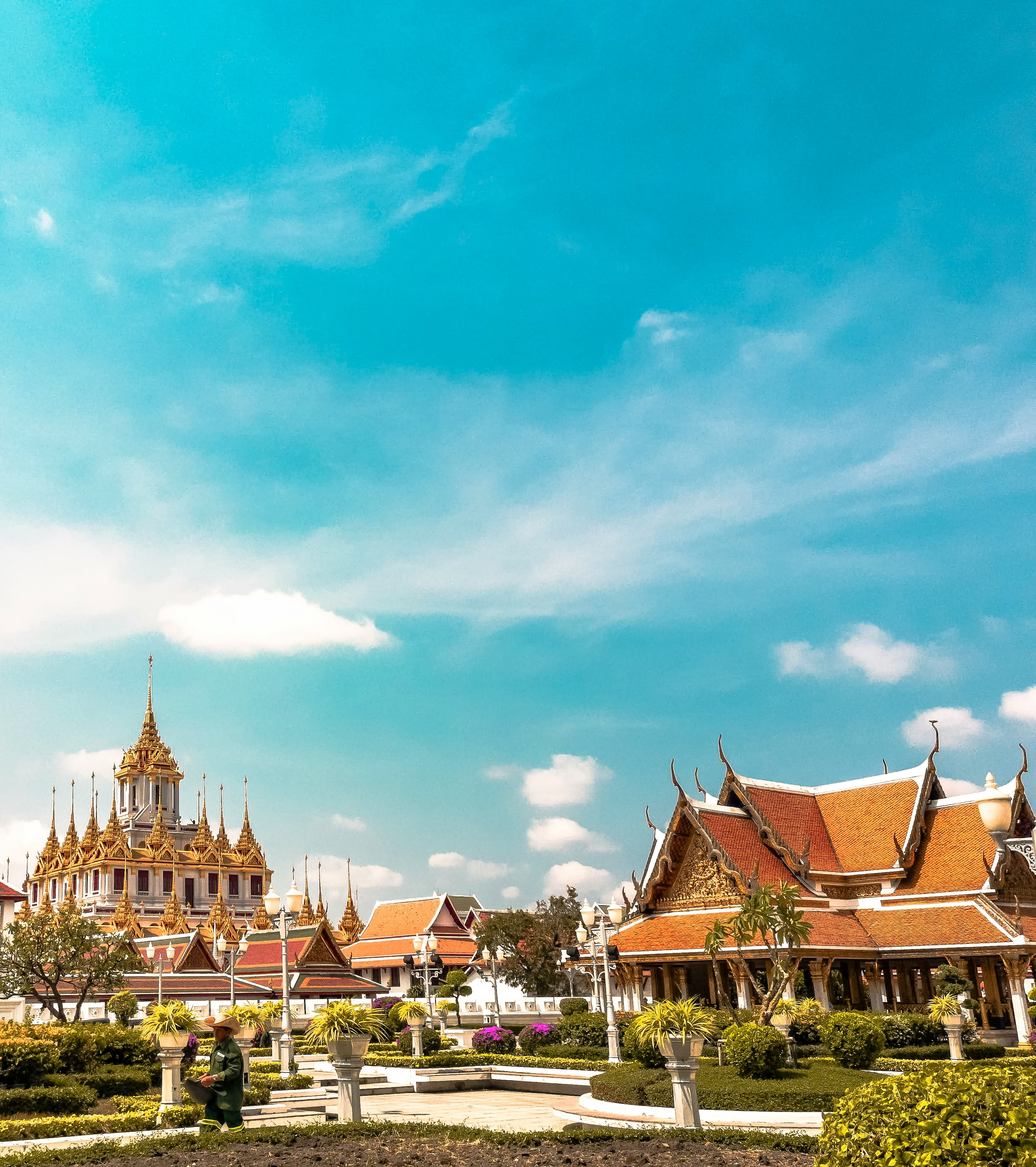 A view of several temples in Bangkok, Thailand against a clear blue sky with a few dotted clouds.