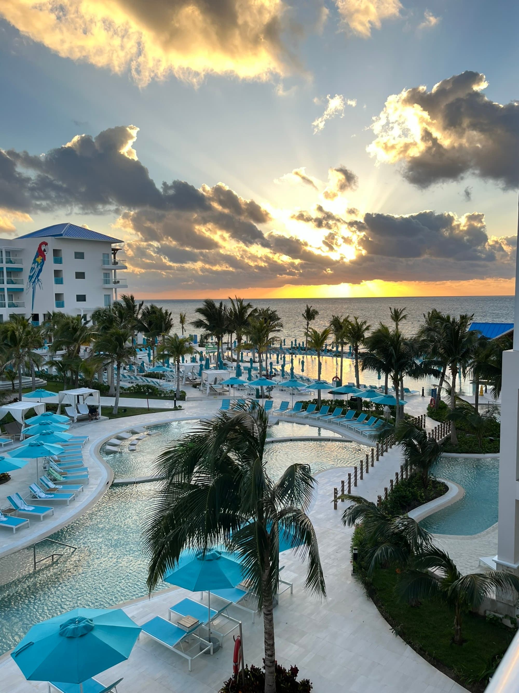 The image shows a sunset view over a resort with a pool and palm trees at sunset.