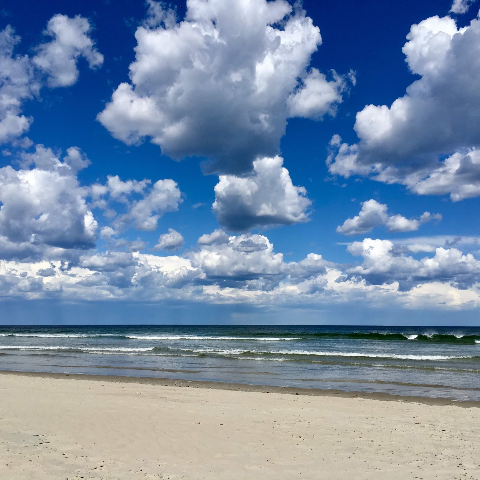 The image shows a serene beach scene with fluffy clouds in the sky and gentle waves on the shore.