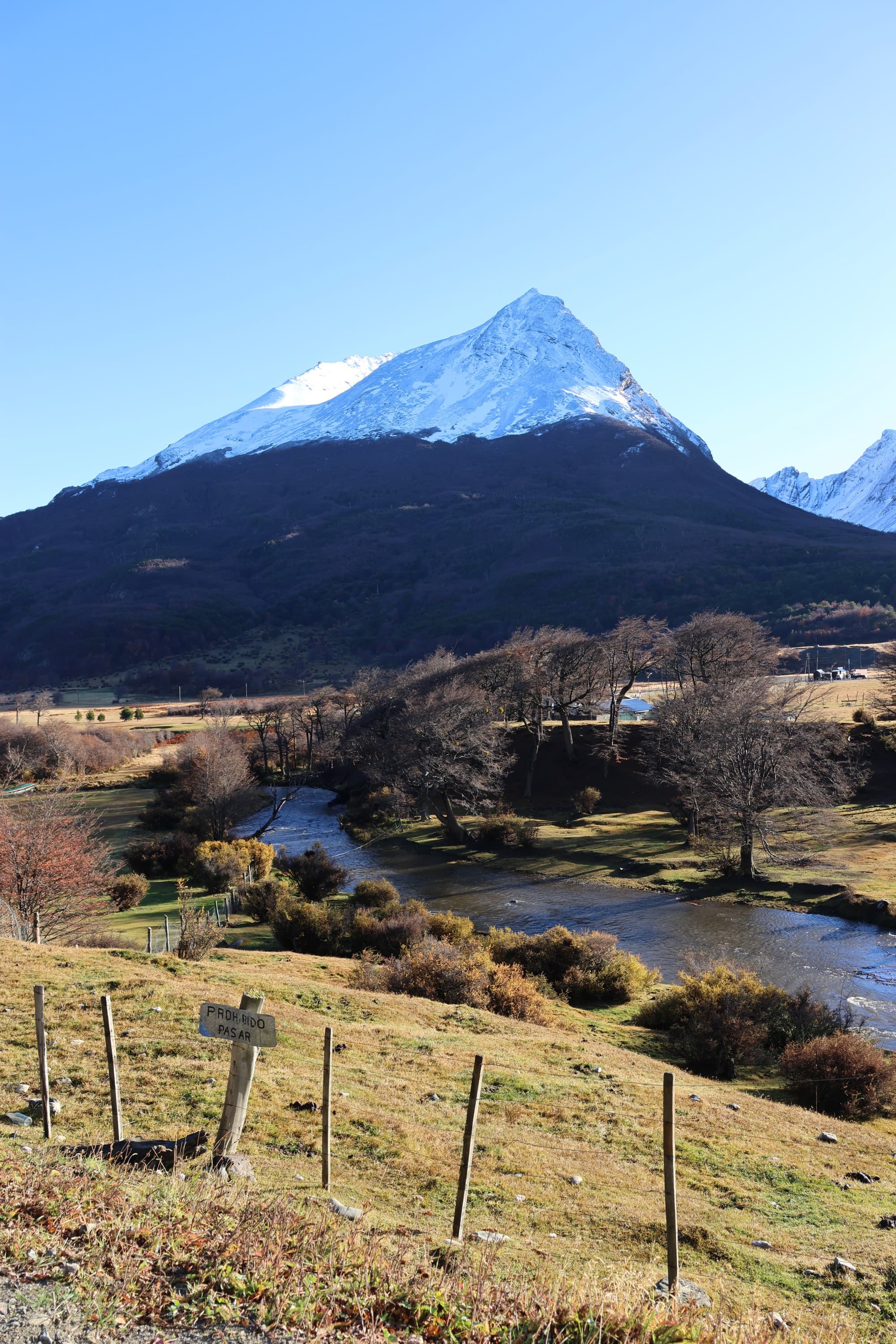 The image captures a breathtaking view of a snow-capped mountain peak, with a serene river flowing through the lush green landscape at its base.