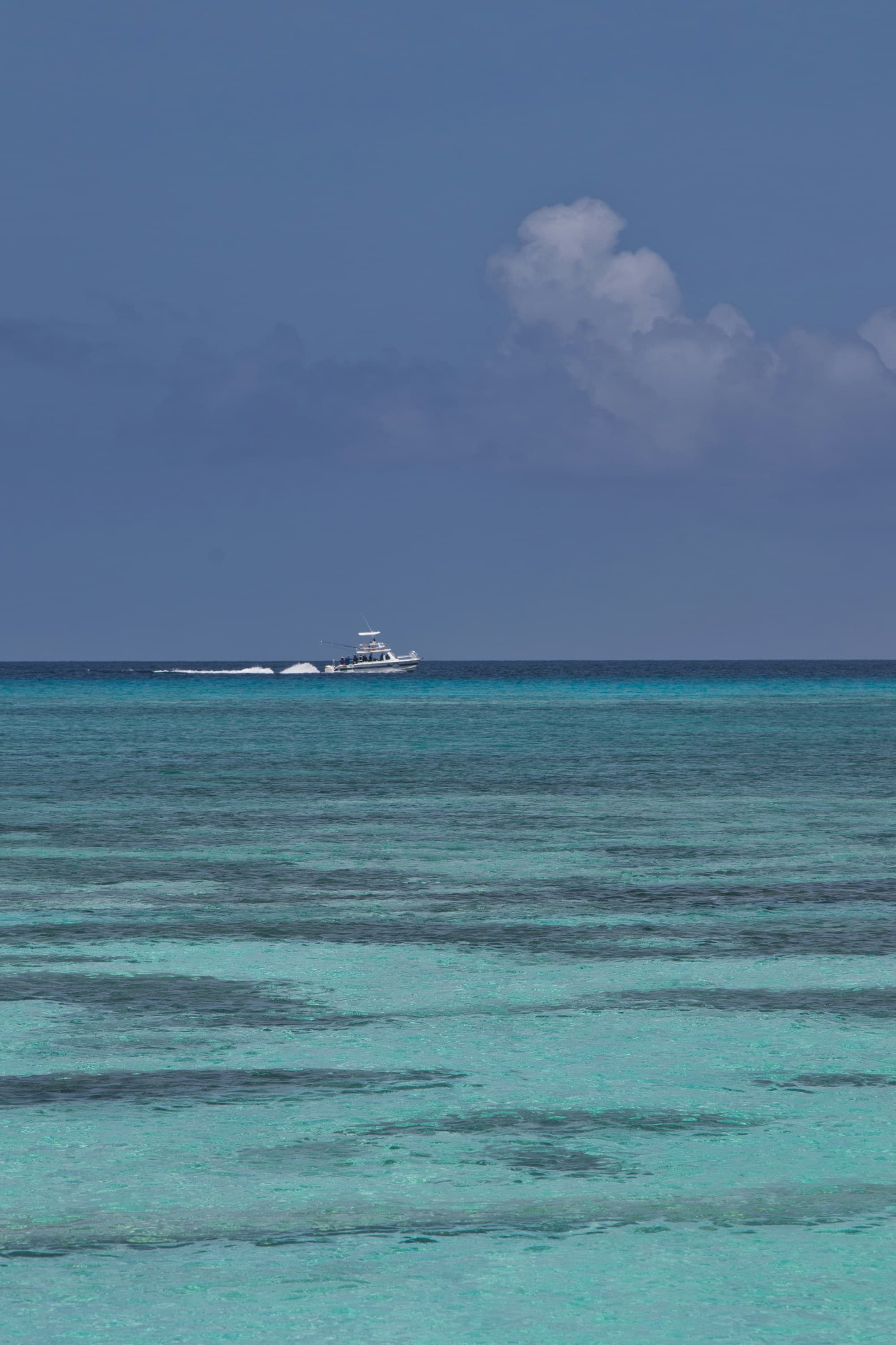 Different shades of turquoise ocean with blue sky and a boat in the far distance.