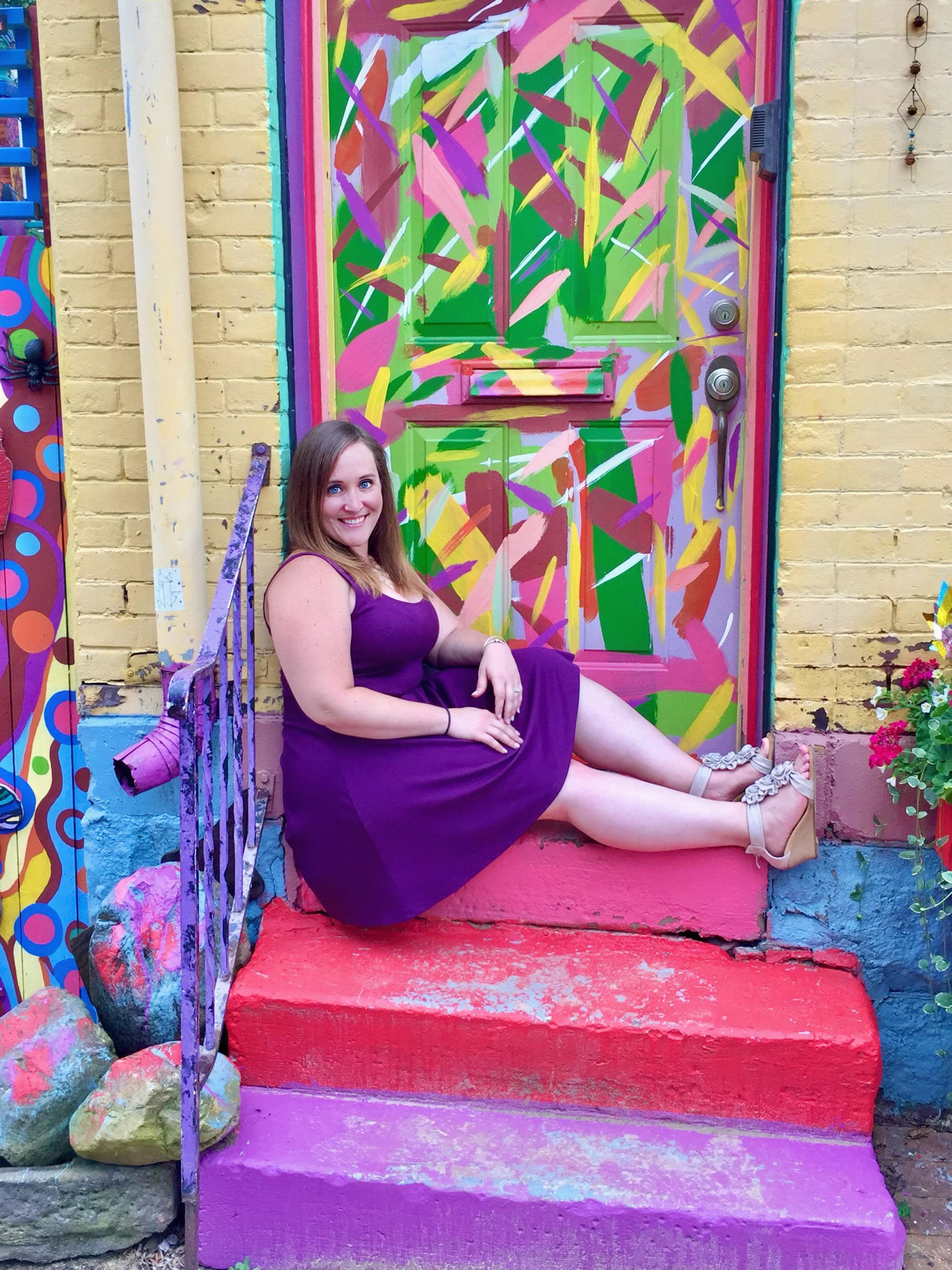 Advisor posing in purple dress sitting on red stairs in front of a colorful mural.