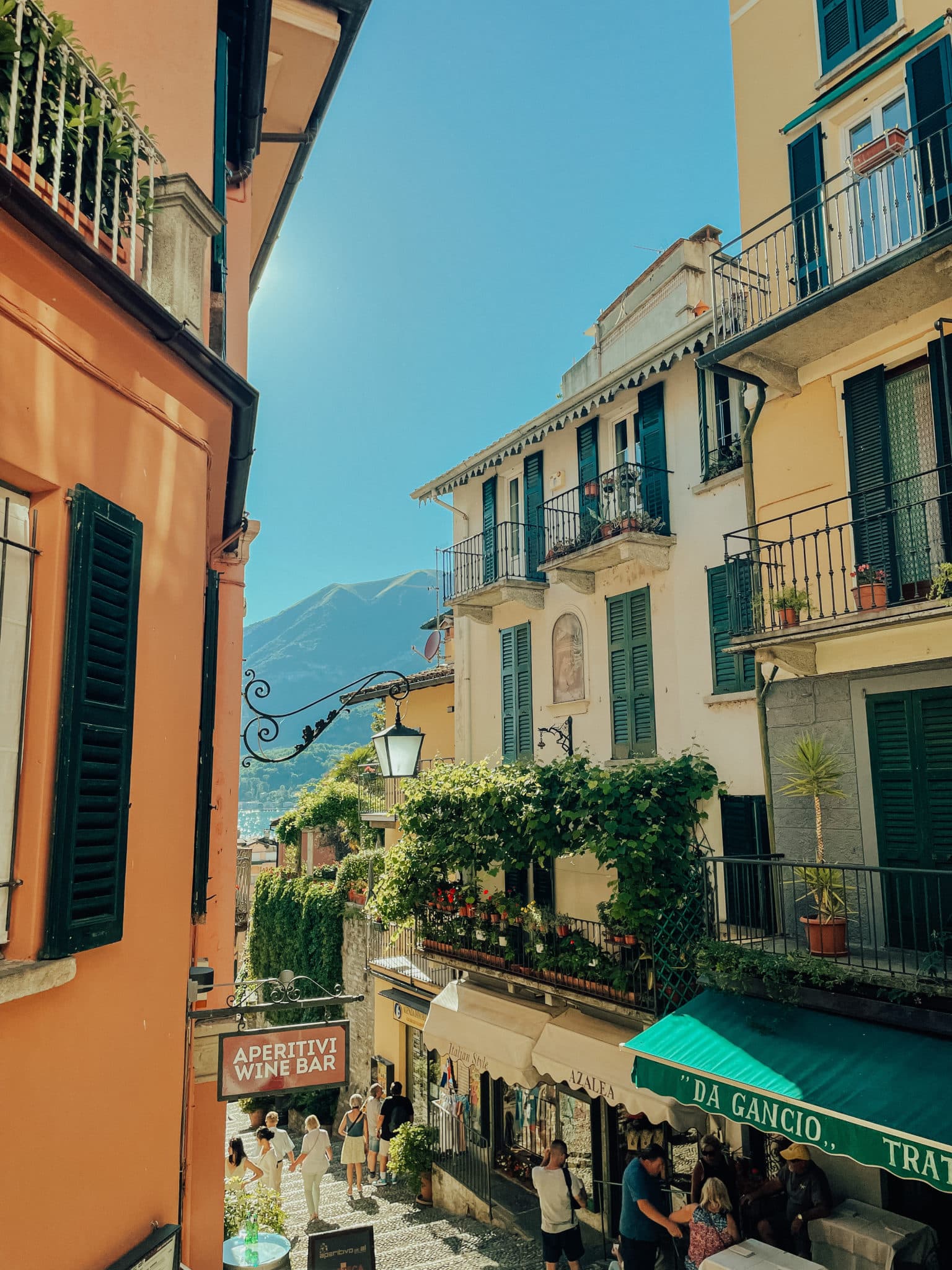 The village of Bellagio unfolds its winding street toward Lake Como as quaint balconied buildings stand tall in the sunshine.