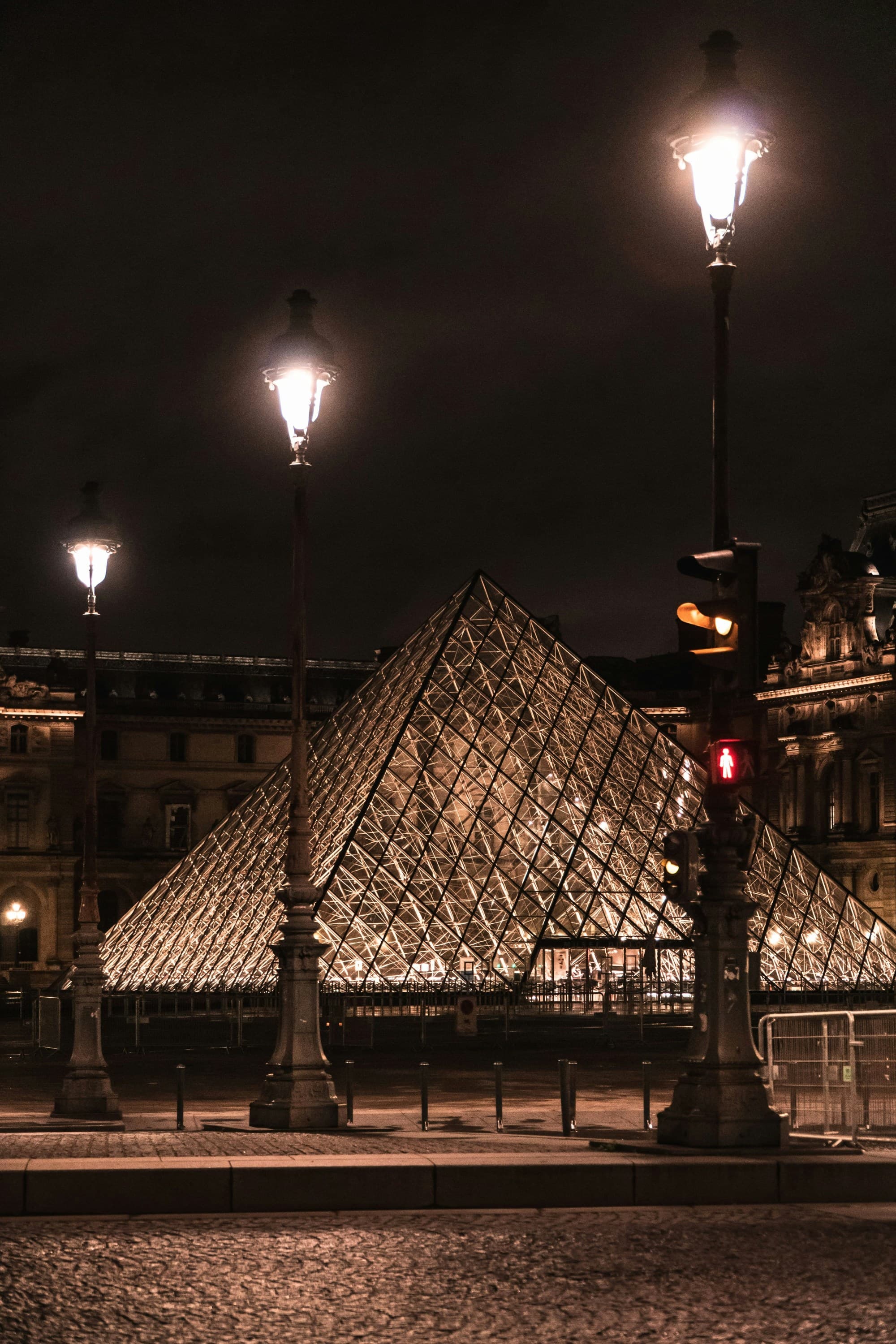 The image features the Louvre Pyramid at night, strikingly lit up against the dark sky.