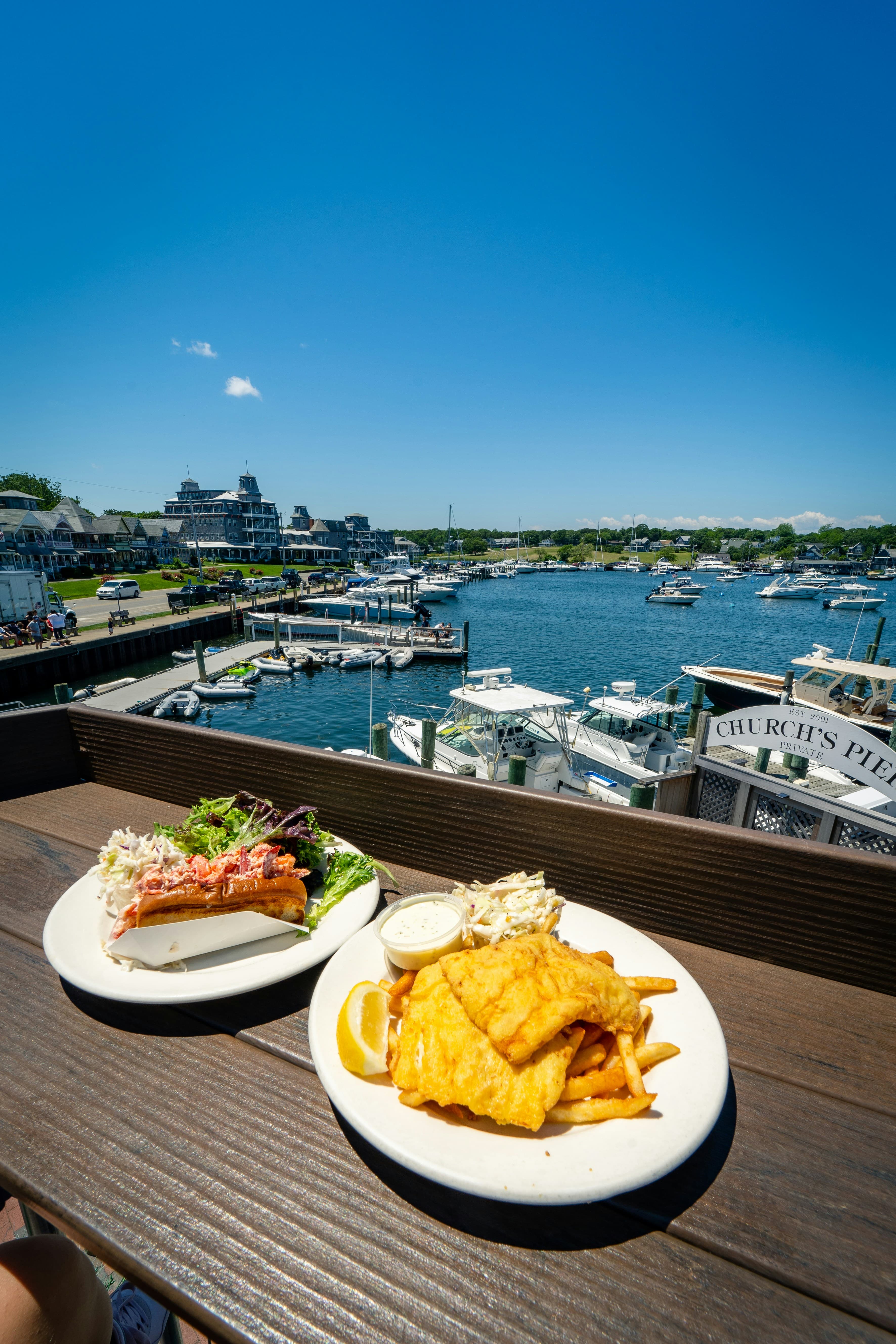 A view of two plates of food on a ledge overlooking a marina with boats docked on a sunny day.