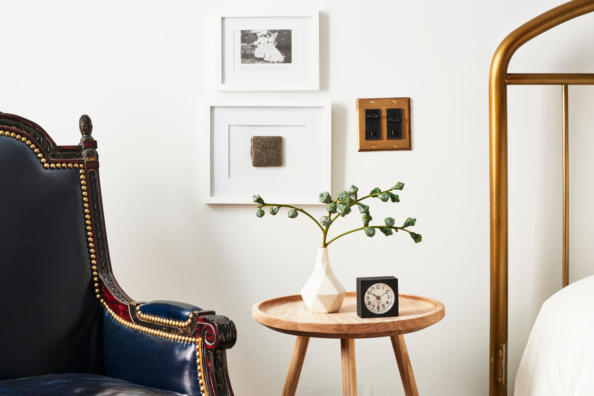 a clock and a potted plant sit on a wooden side table next to a bed