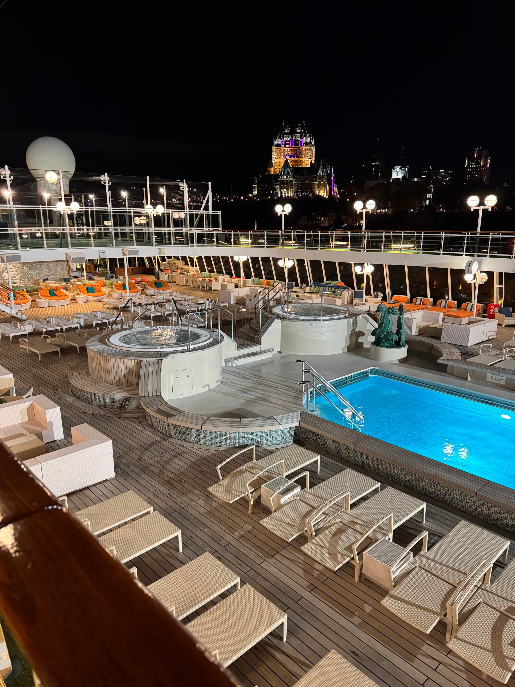 A swimming pool area surrounded by lounge beds and seating at nighttime
