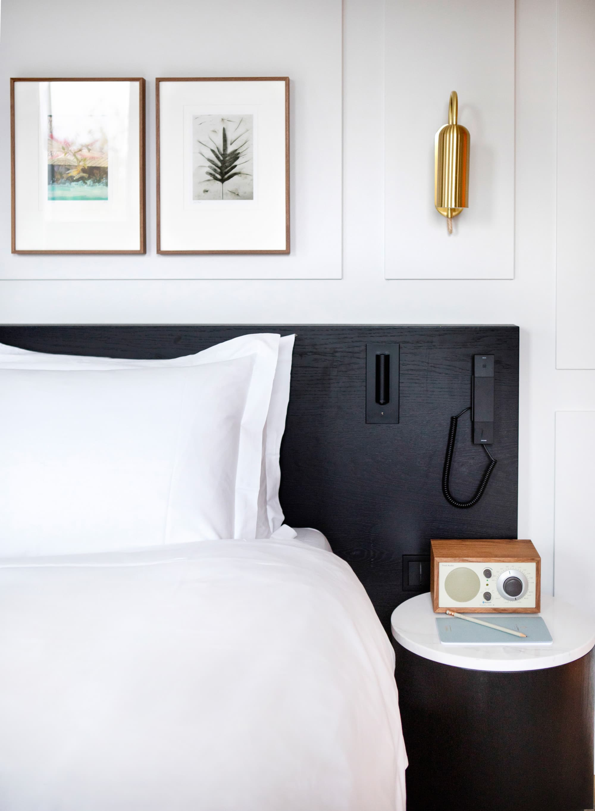 close-up of a white bed with a black headboard next to a wooden end table with an old-fashioned radio