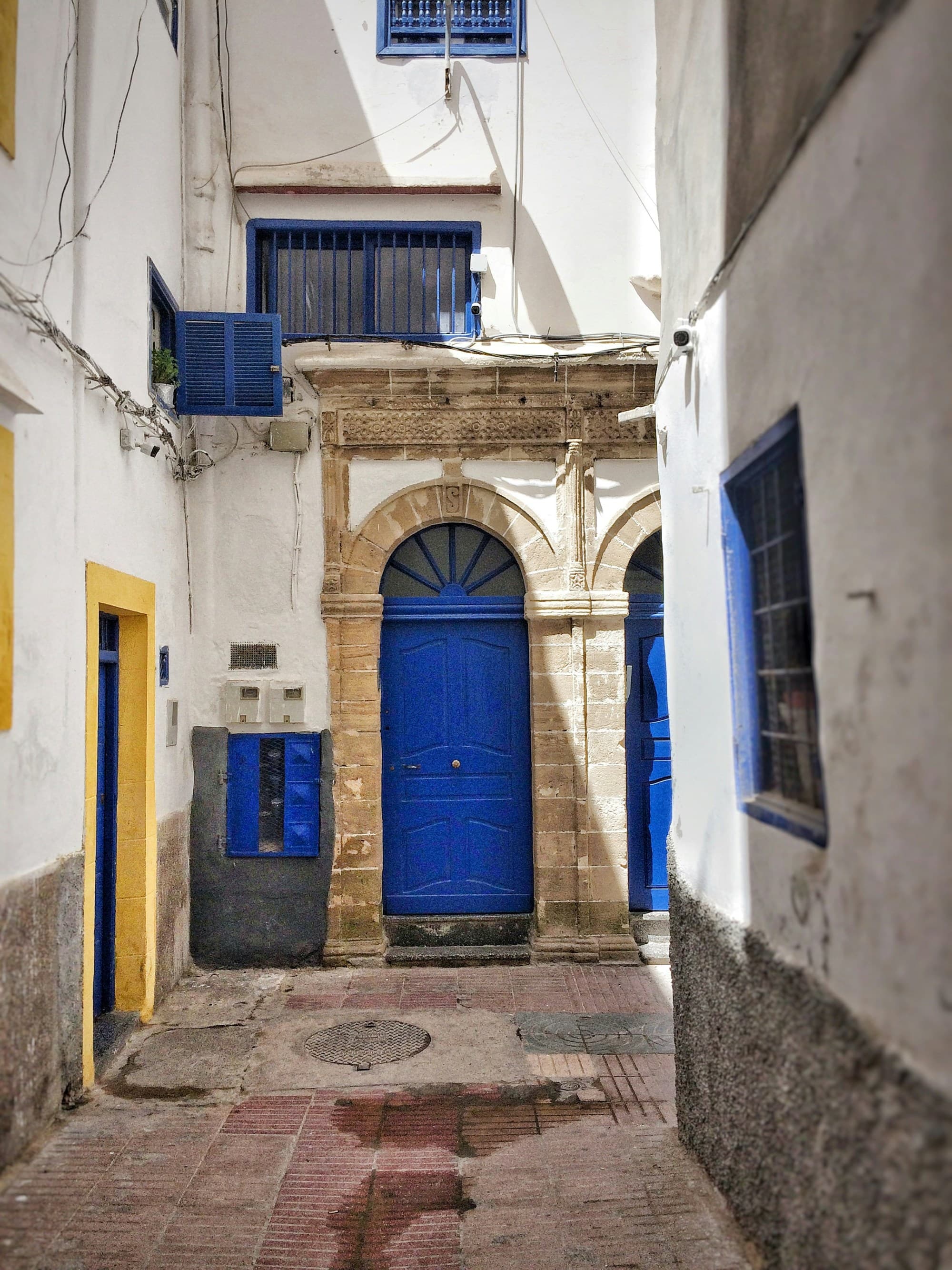A quaint white-walled stone alleyway with a striking blue door and windows.