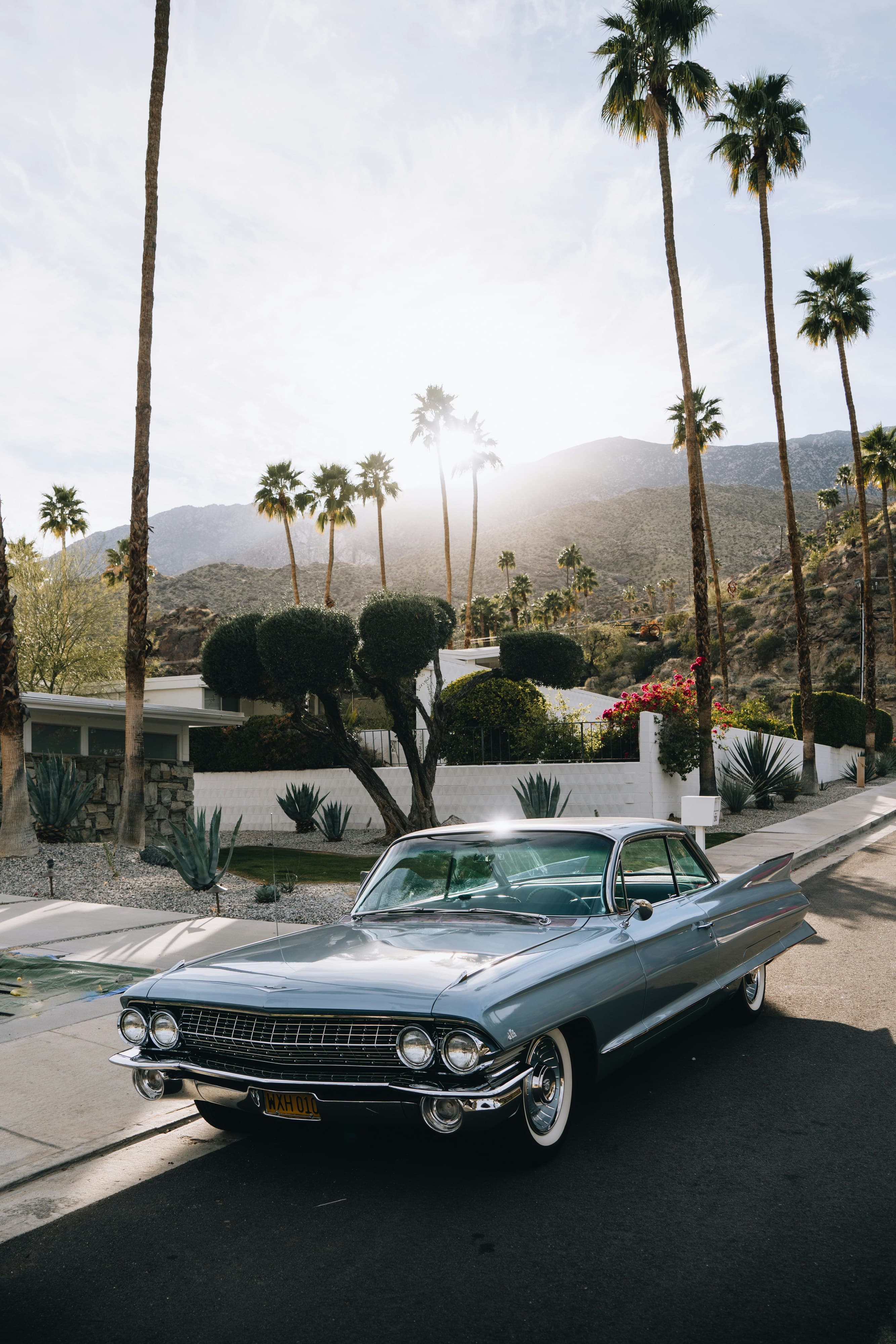 A classic sky blue car parked on the street in Palm Springs with palm trees and a mountain scape in the distance.