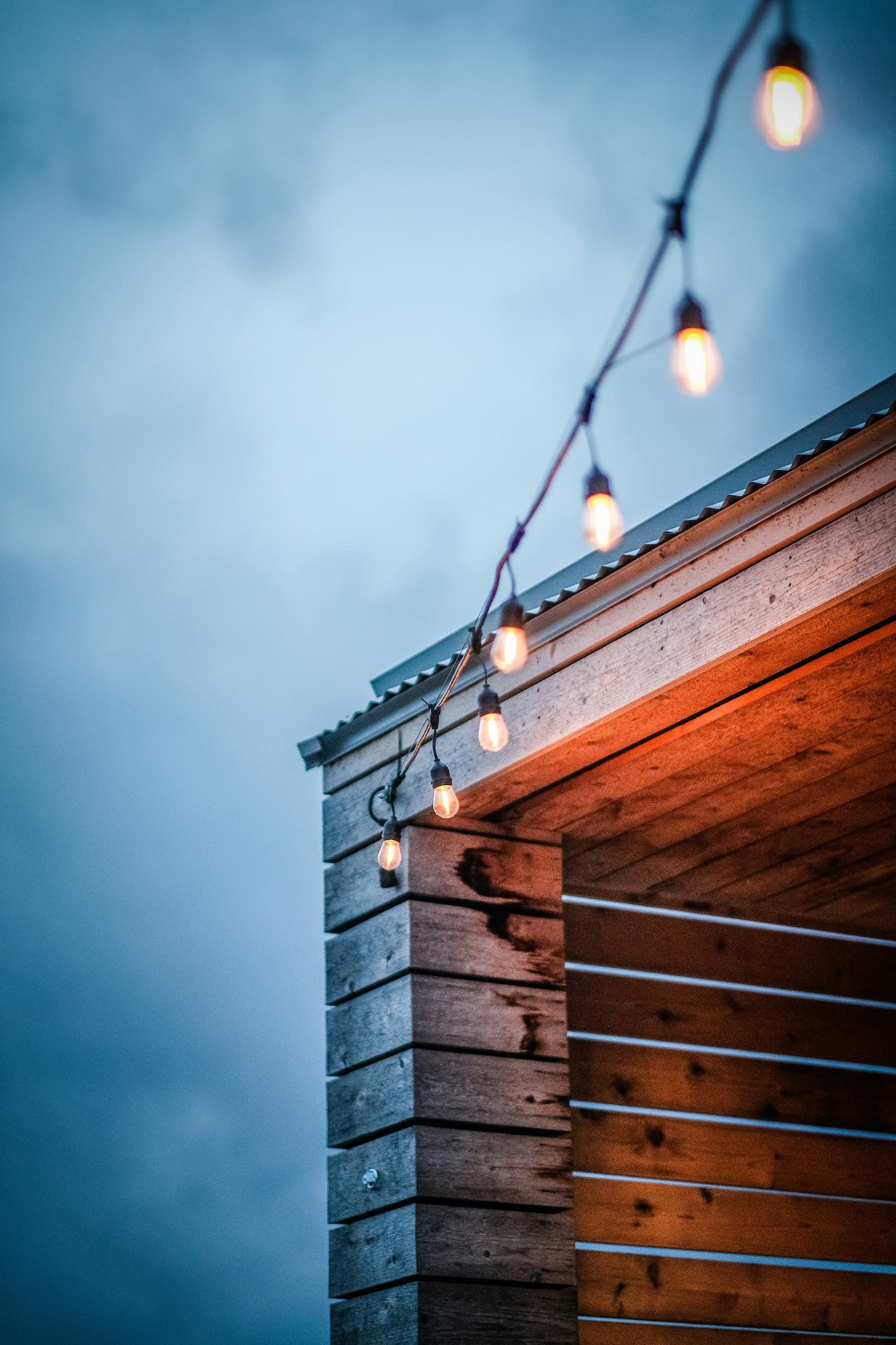 Bulb lights hanging from roof of a building on an overcast evening.