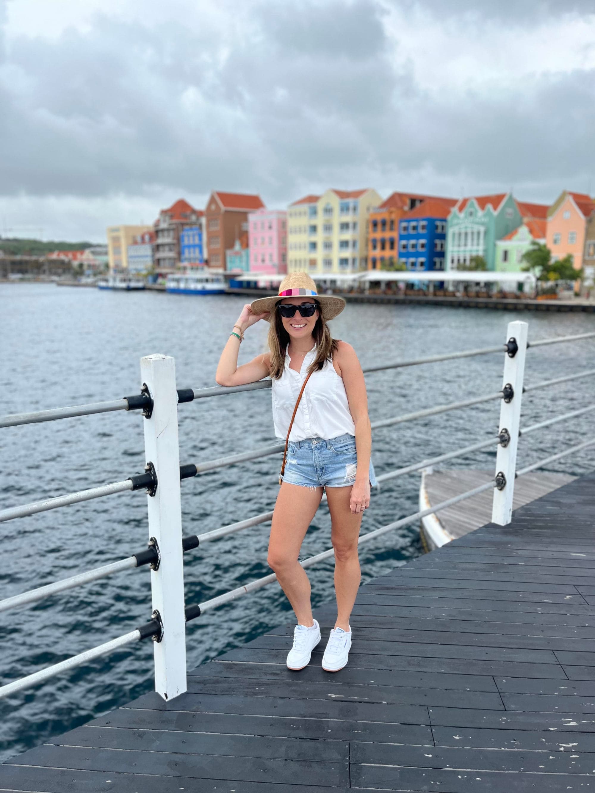 A woman standing in front of waterbody with colorful buildings in the distance.