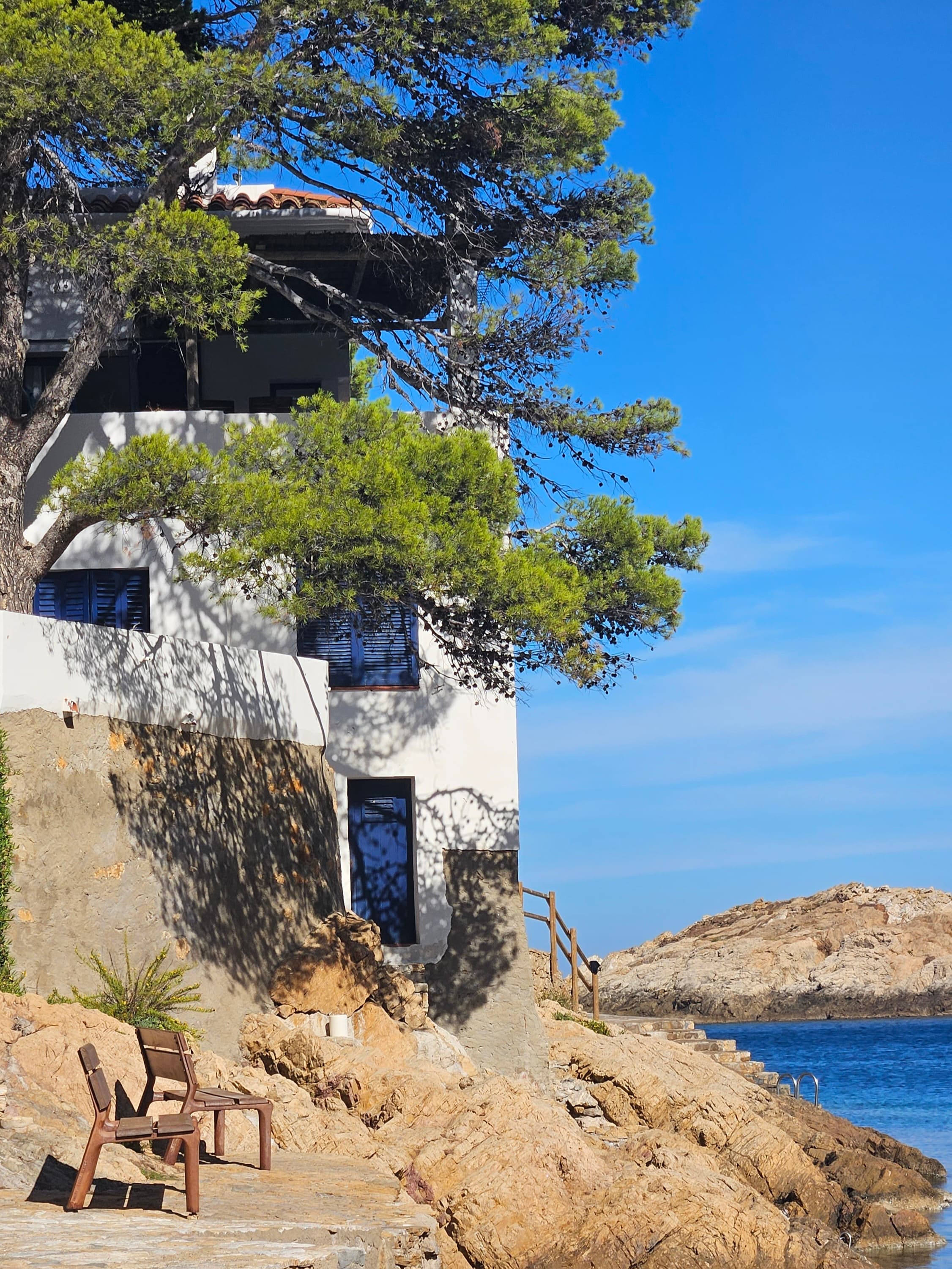 A white and blue house built into the rocky terrain on the coast of Begur, on a sunny day in Spain.