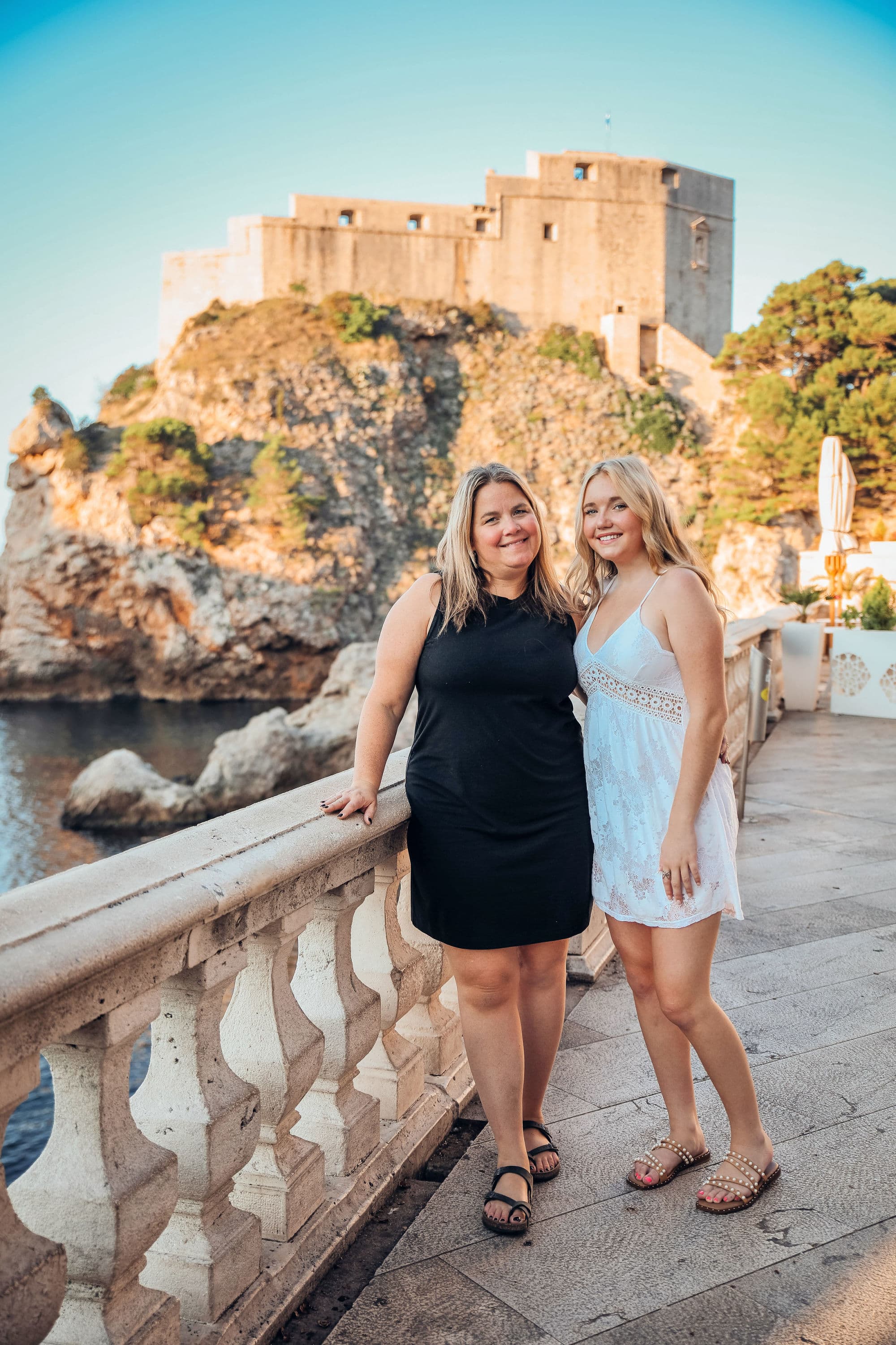 Two women standing and posing for a photo on a bridge over a body of water