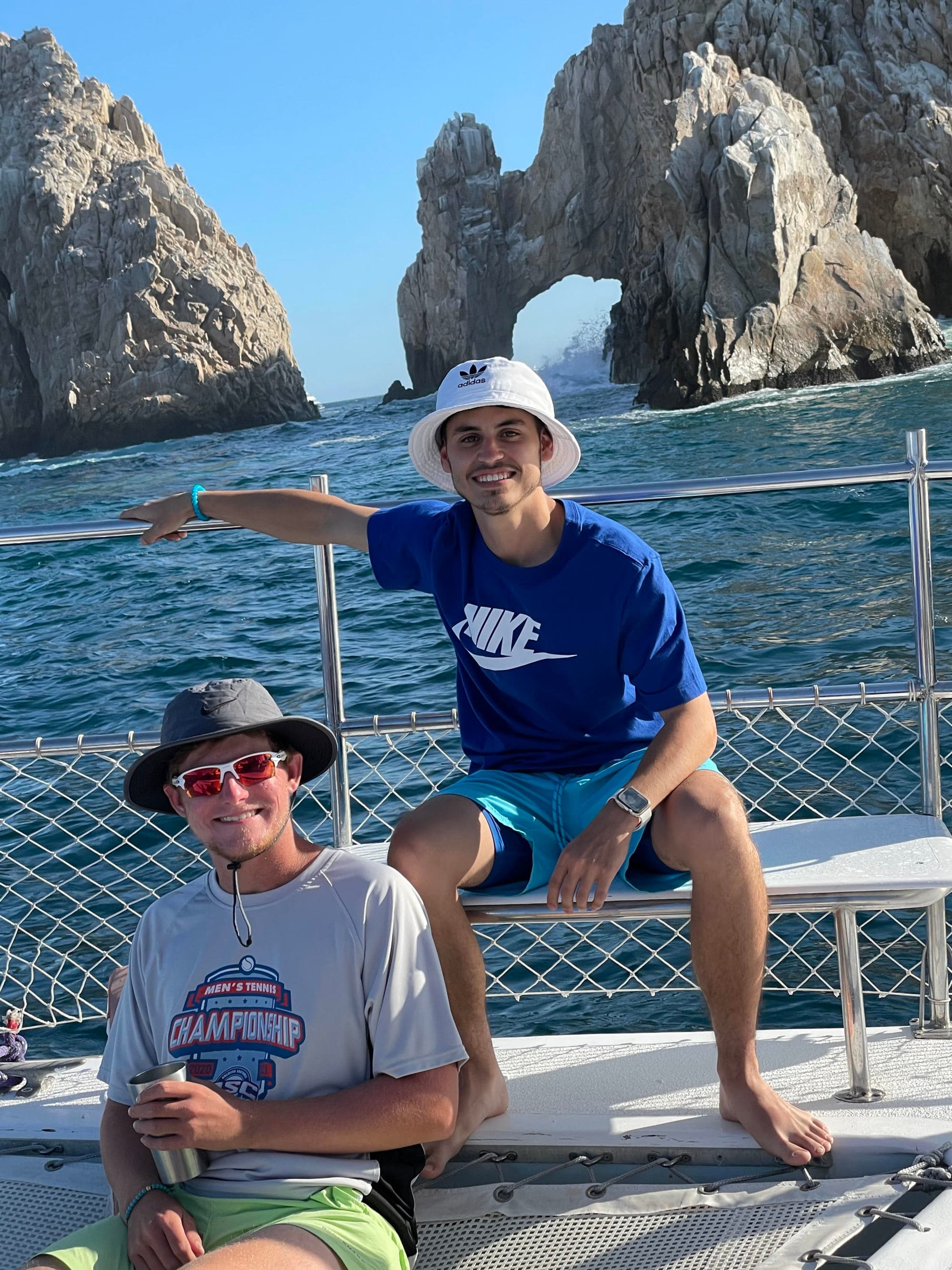 Two individuals on a boat, with rocky formations and the ocean in the backdrop.