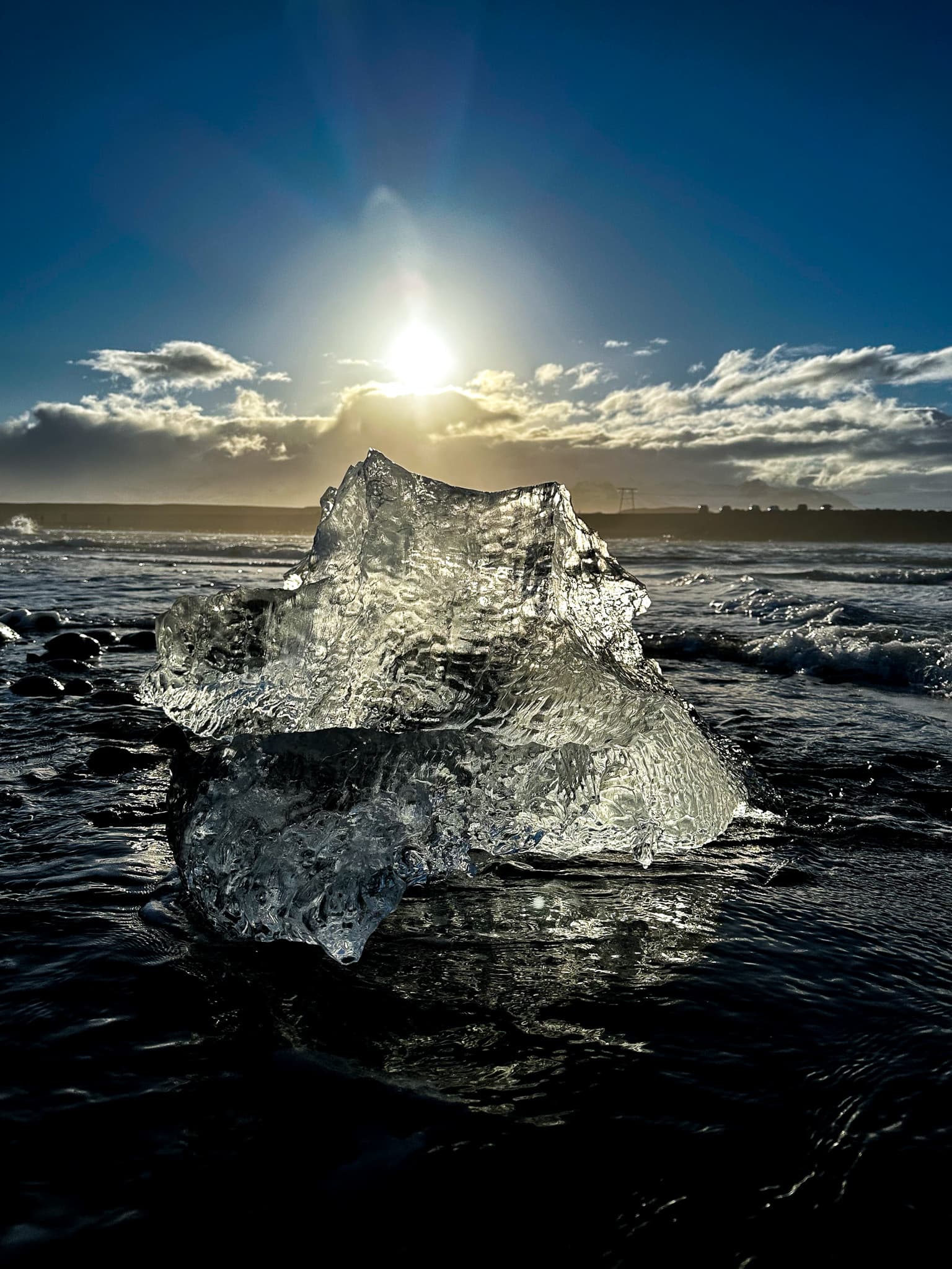 A spiky block of ice in the water with the sun setting over the horizon.