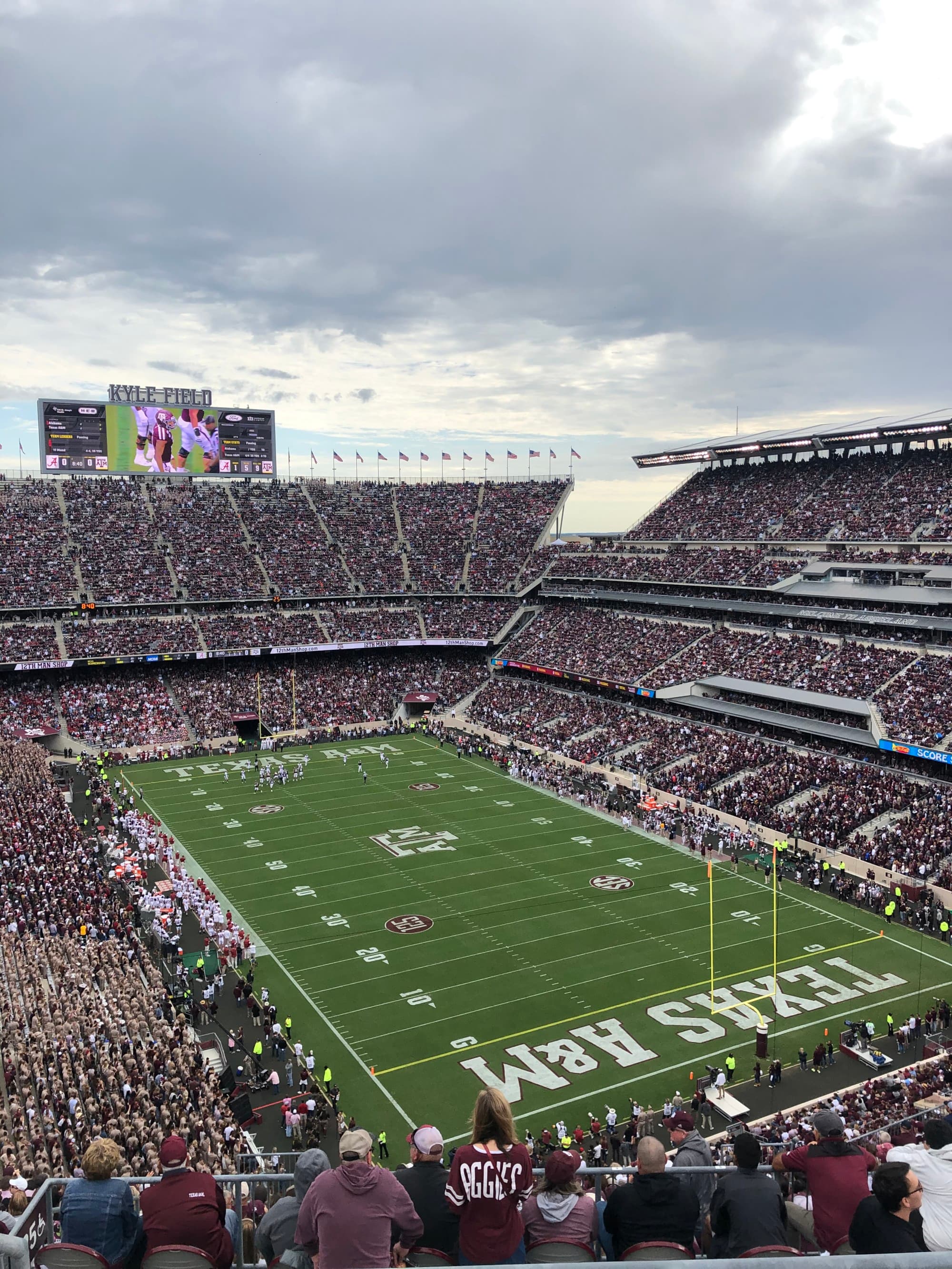 The image showcases an overcast day at a packed stadium with a view of the field and “TEXAS A&M UNIVERSITY” prominently displayed.