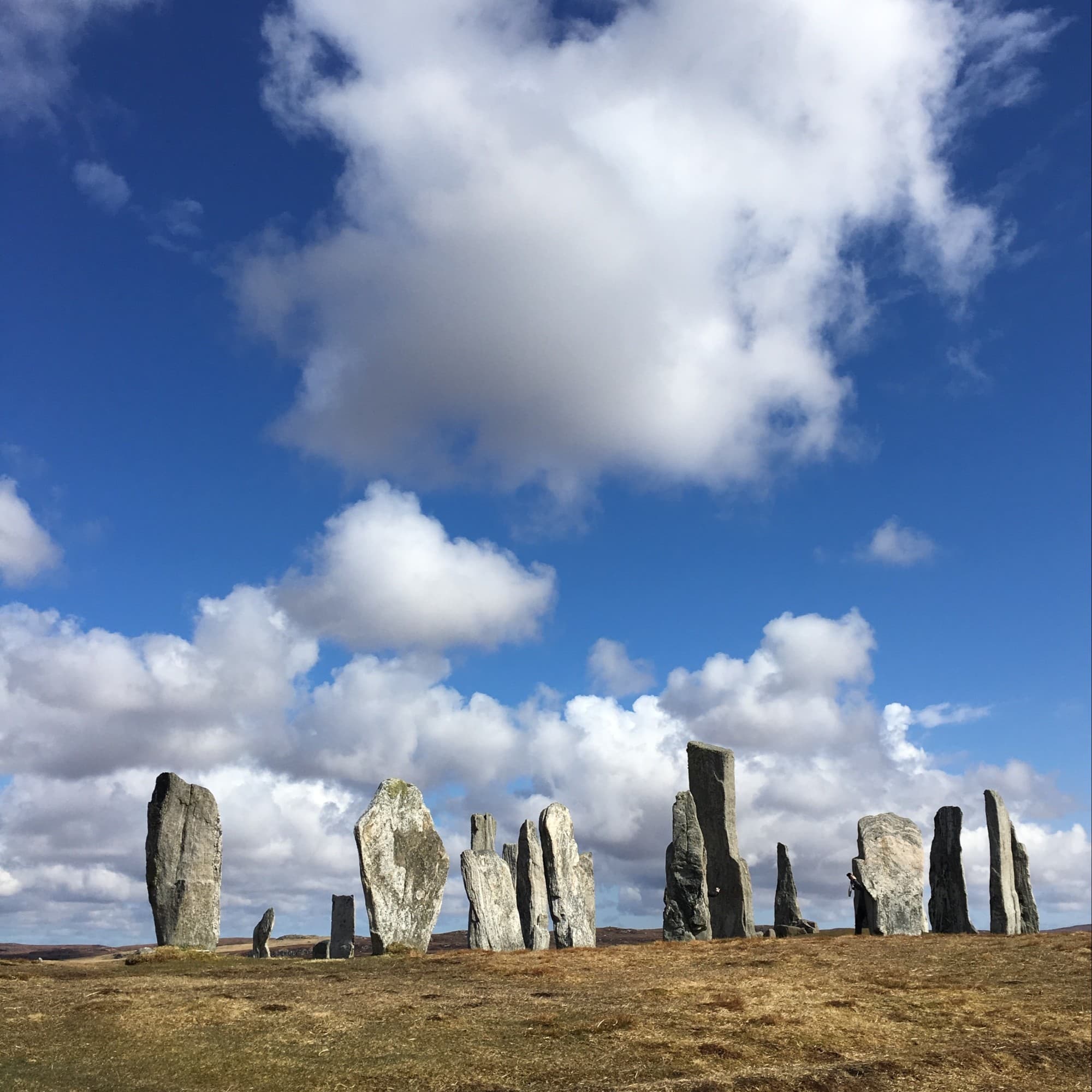 Tall, slender standing stones against a blue sky with scattered clouds.