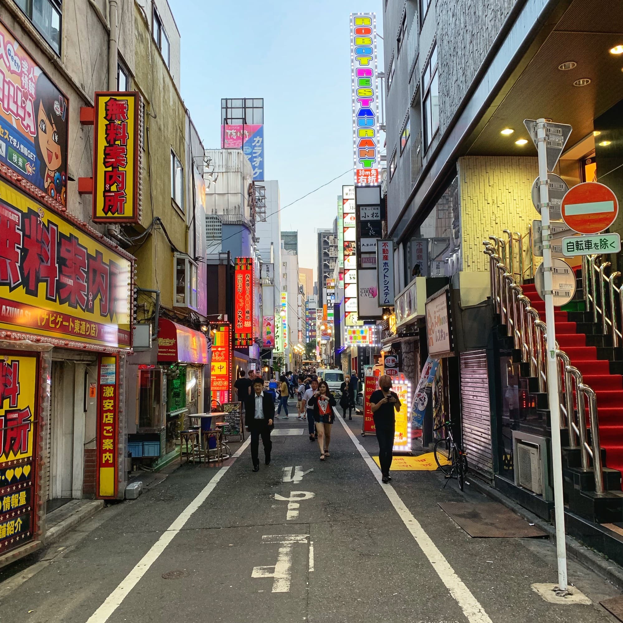 A vibrant Japanese street at dusk, illuminated by the glow of colorful signs and billboards.