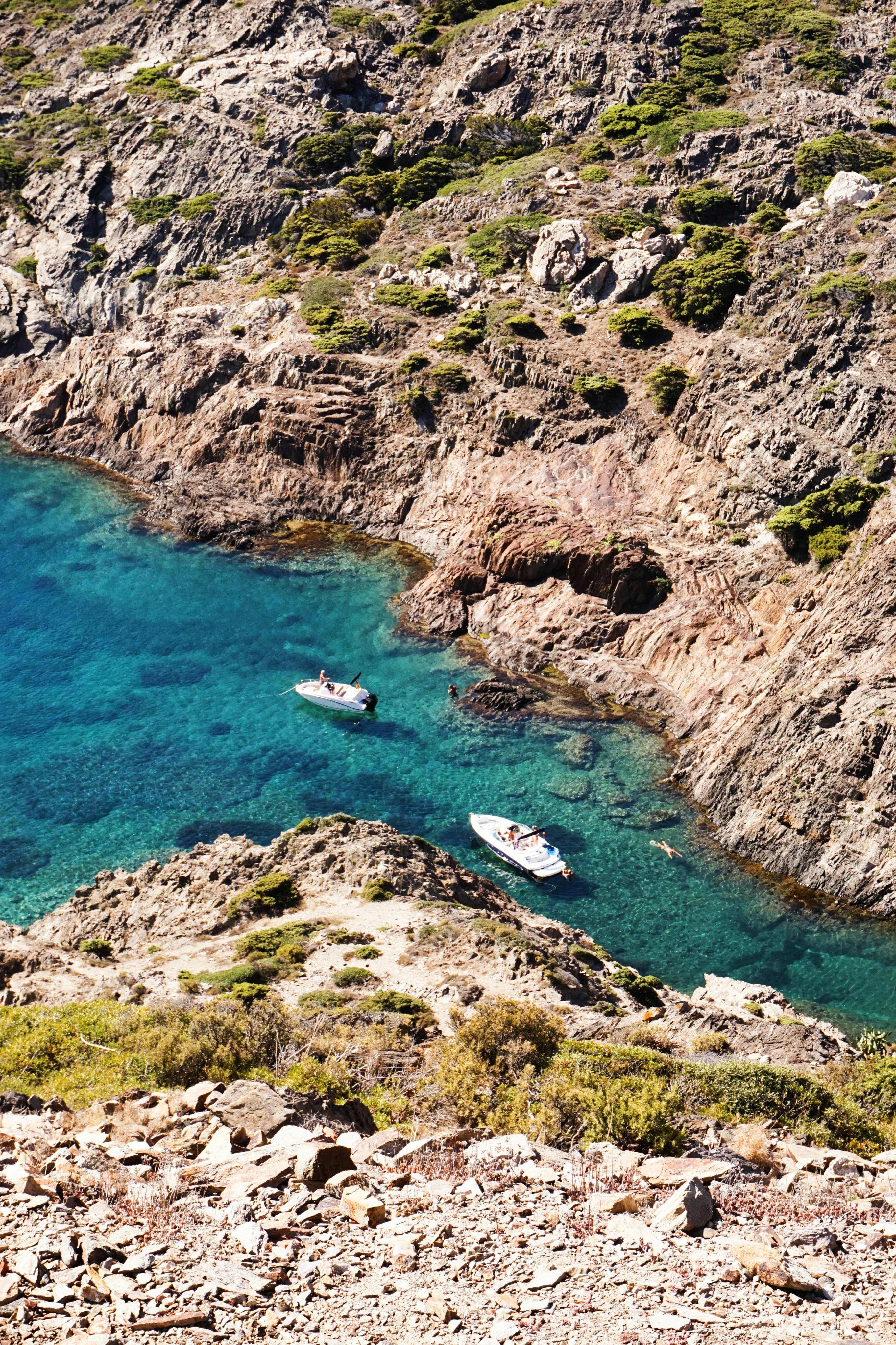 The image portrays a small boat amidst towering cliffs by the sea, under a pale overcast sky.