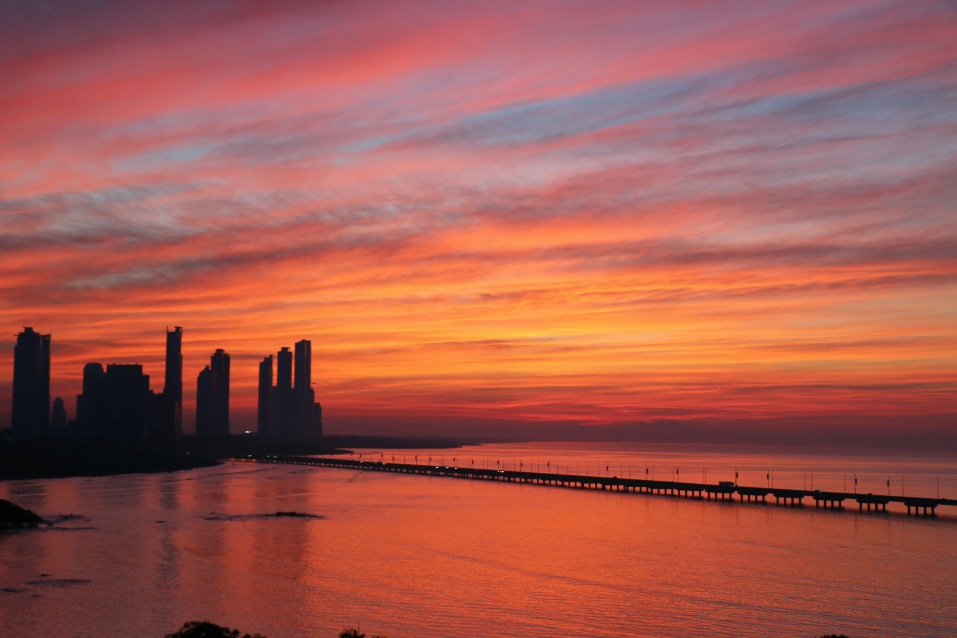 A golden, pink and lavender sunrise over Panama City, over the water and a silhouetted skyline.