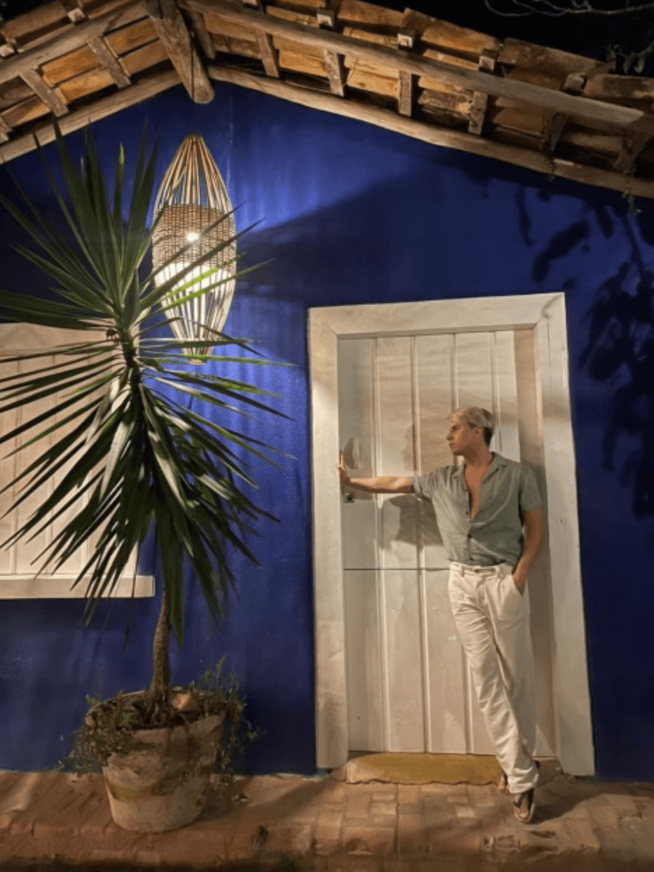 A man earing a green shirt and white pants posing in front of a white doorway and blue wall