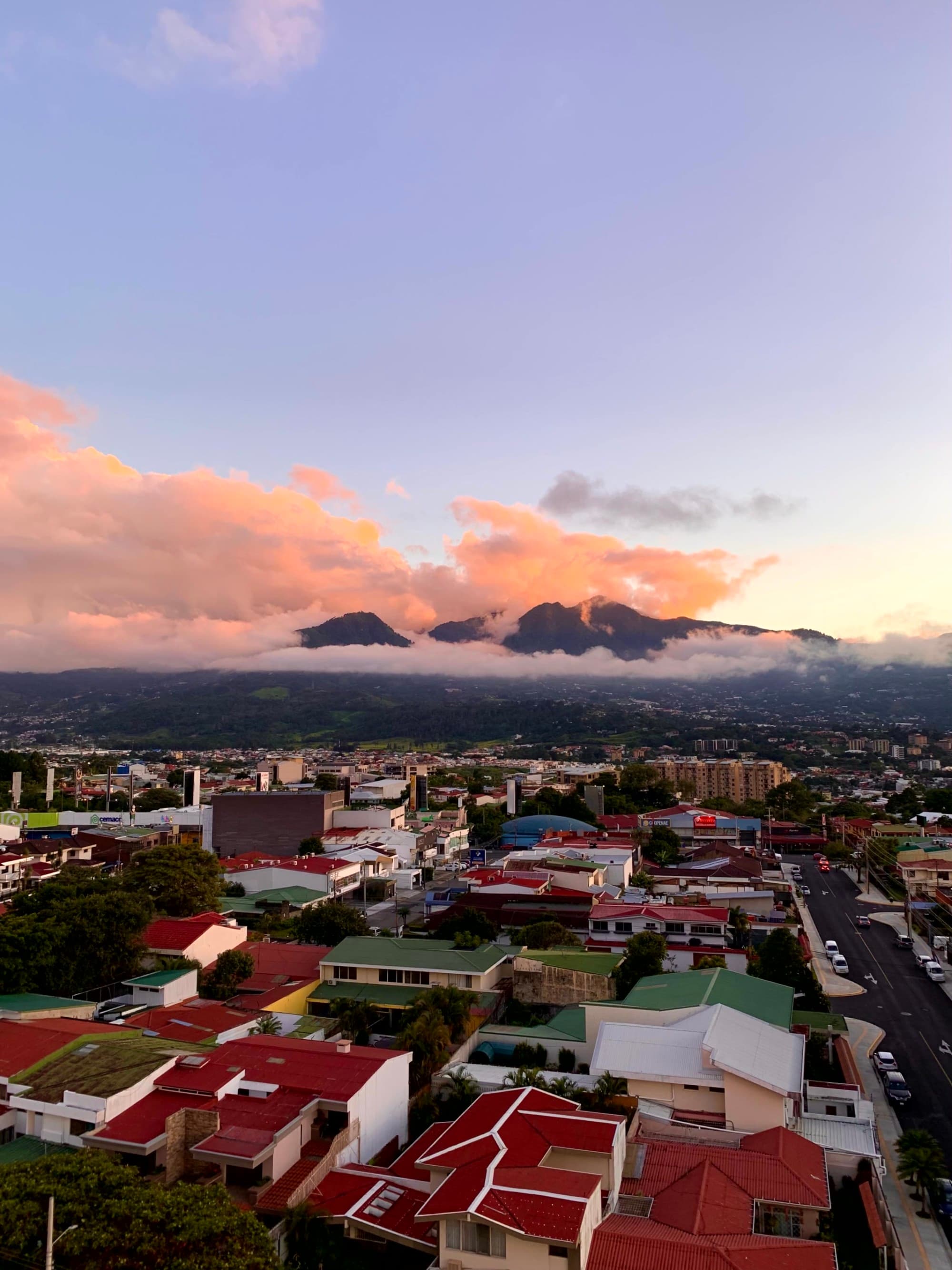 The image presents a cityscape at dusk, with silhouetted mountains and a sky painted in vivid sunset hues.