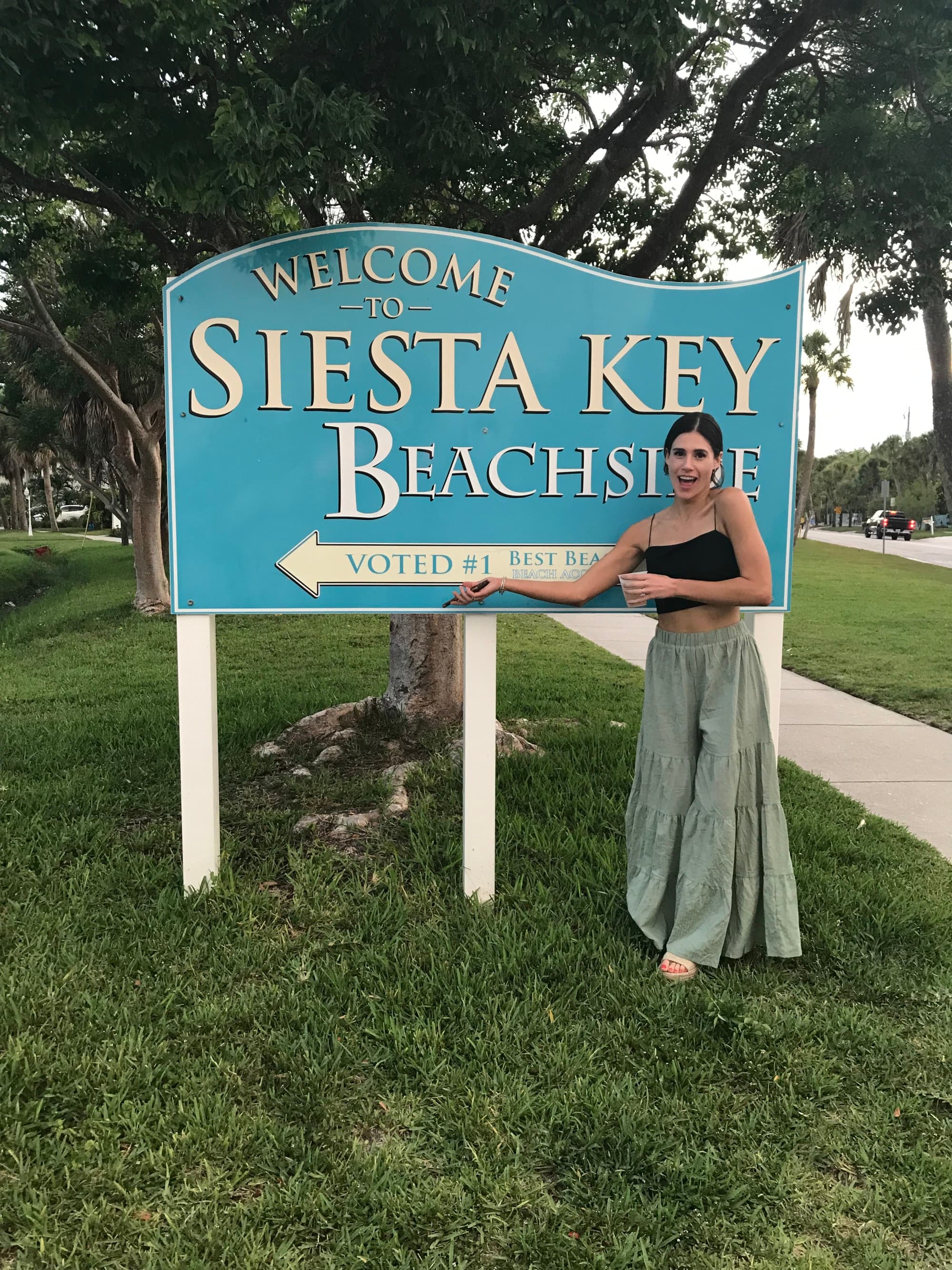 A woman stands before the “Welcome to Siesta Key Beach” sign, hinting at the beach’s allure and hospitality.