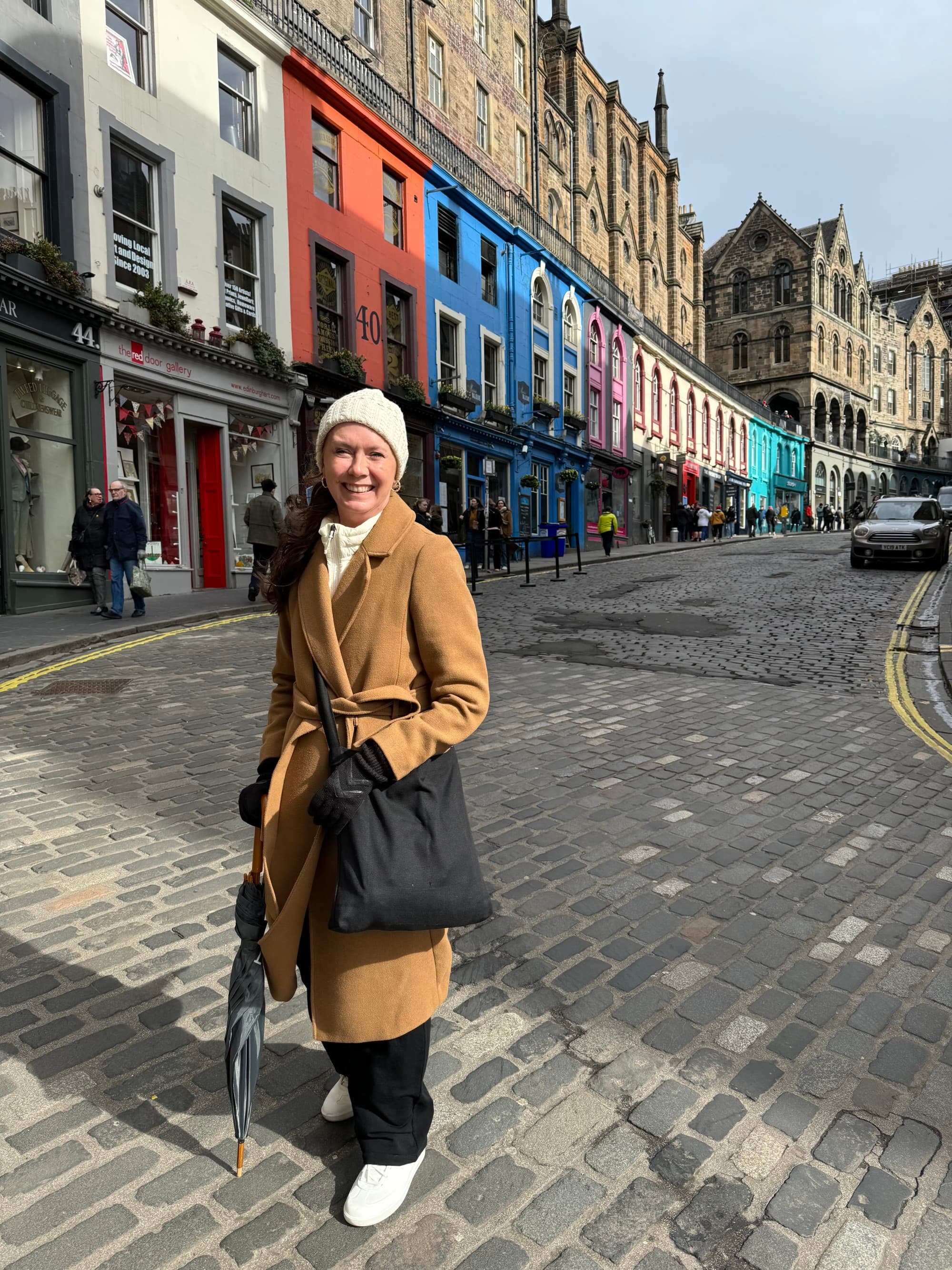 A vibrant urban scene with an Advisor on a cobblestone street during her route from Edinburgh to Glasgow, set against a backdrop of colorful buildings.