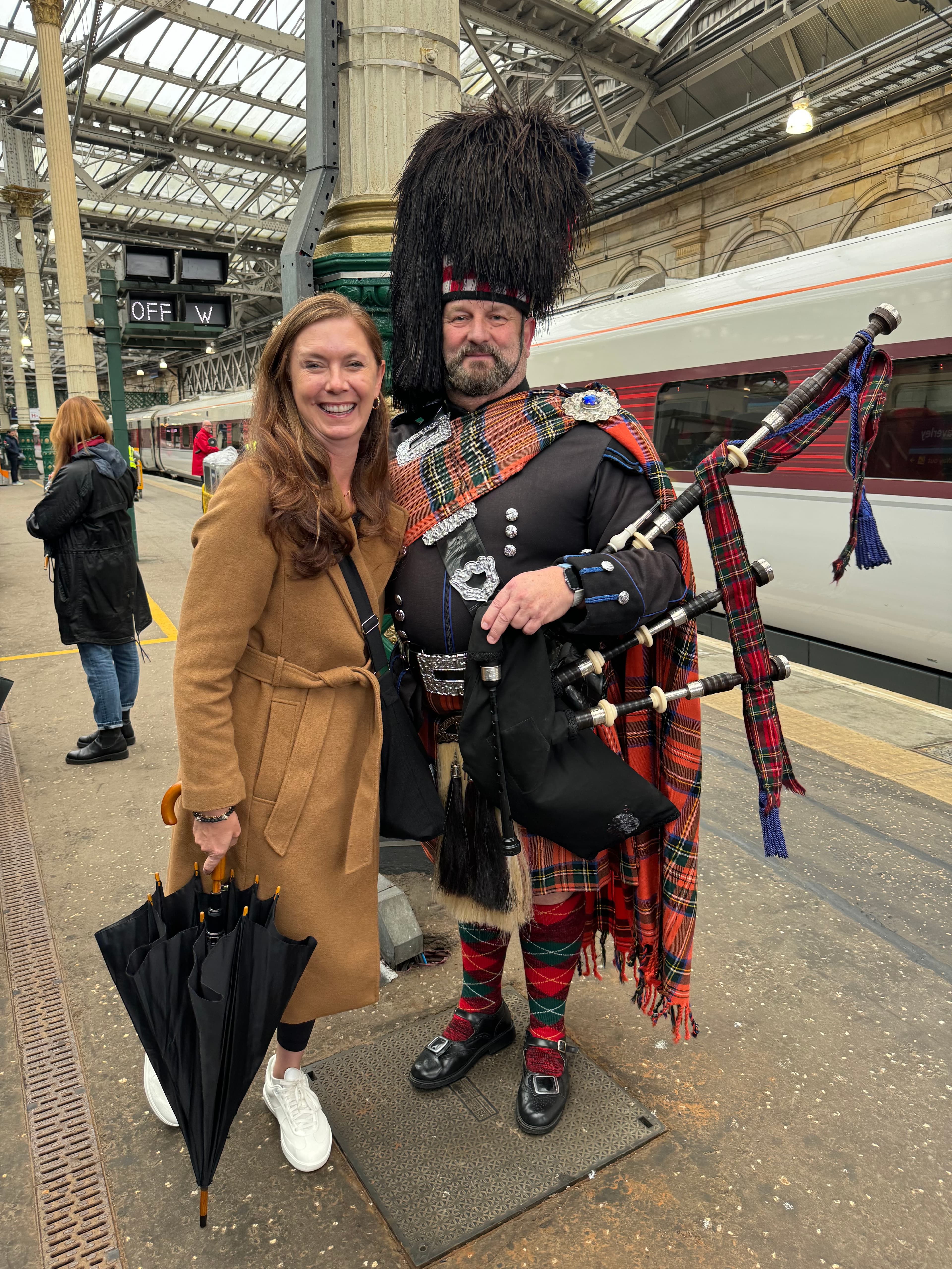 Advisor posing with a bagpipe man on a train platform