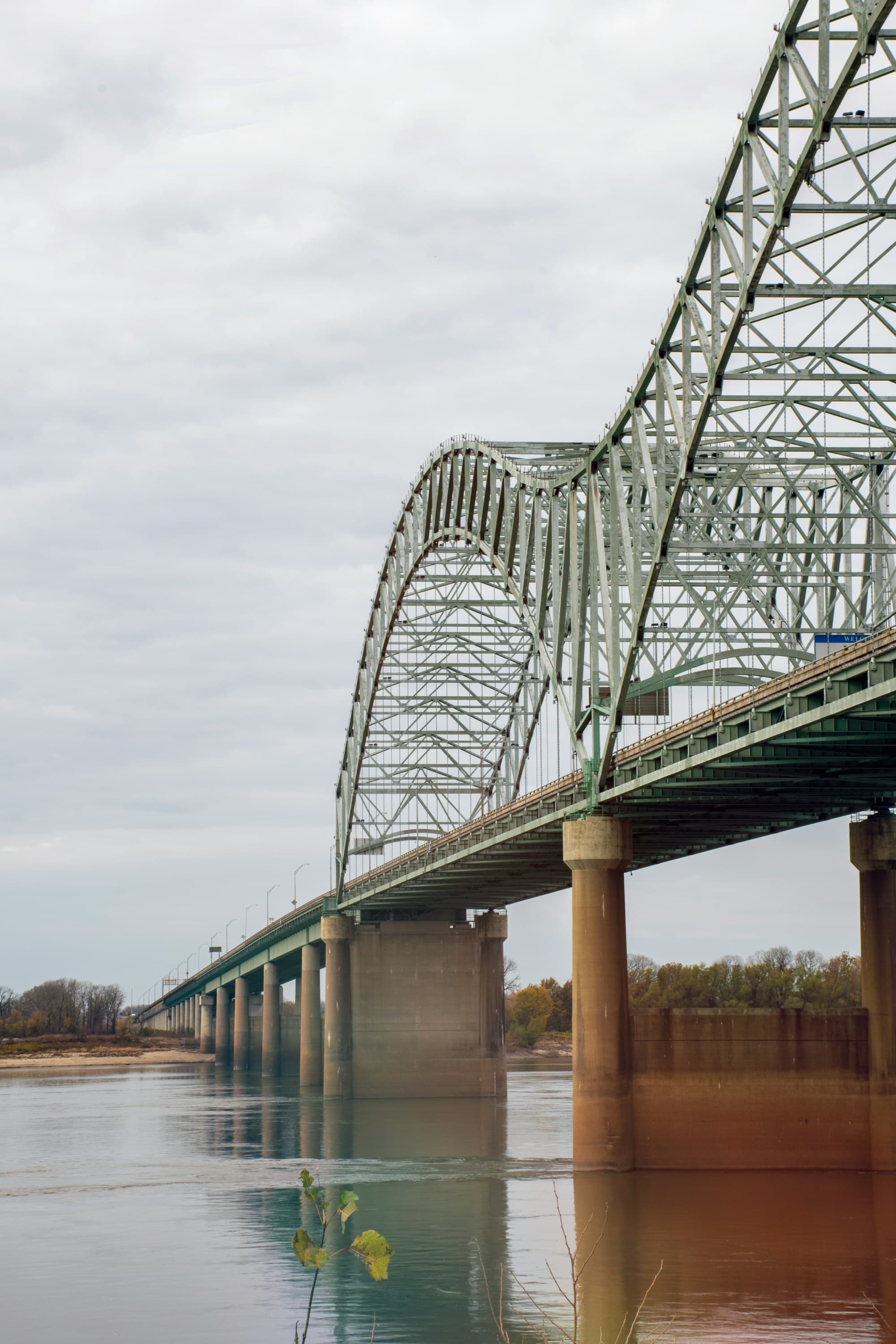 A picture of a grey metal bridge over a river during daytime.