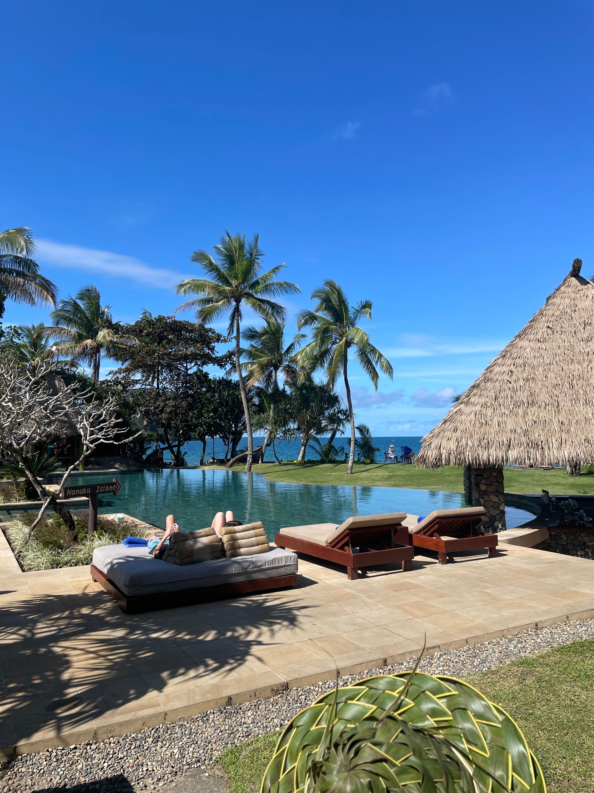 Lounge chairs near a pool next to a hut during daytime.