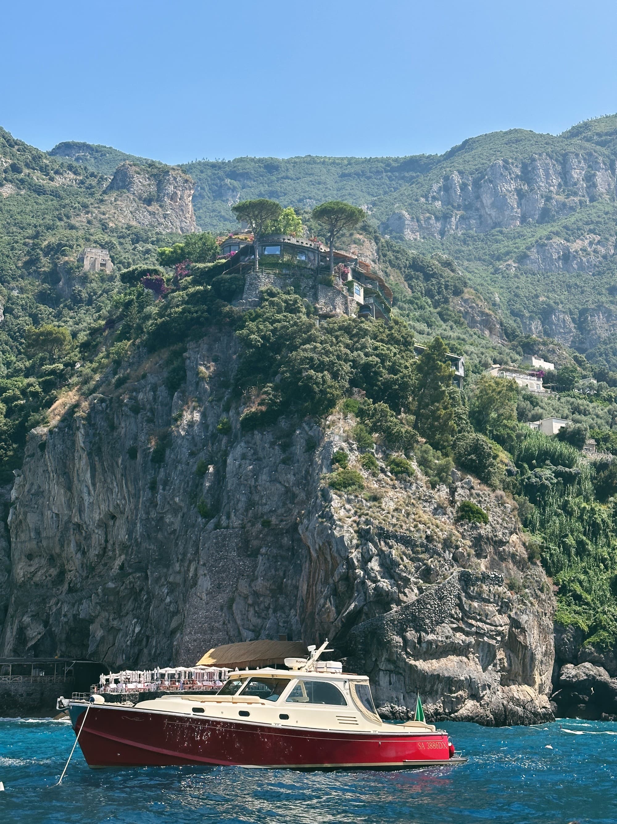 A picture of a red-colored ship on the water near an Island during daytime.