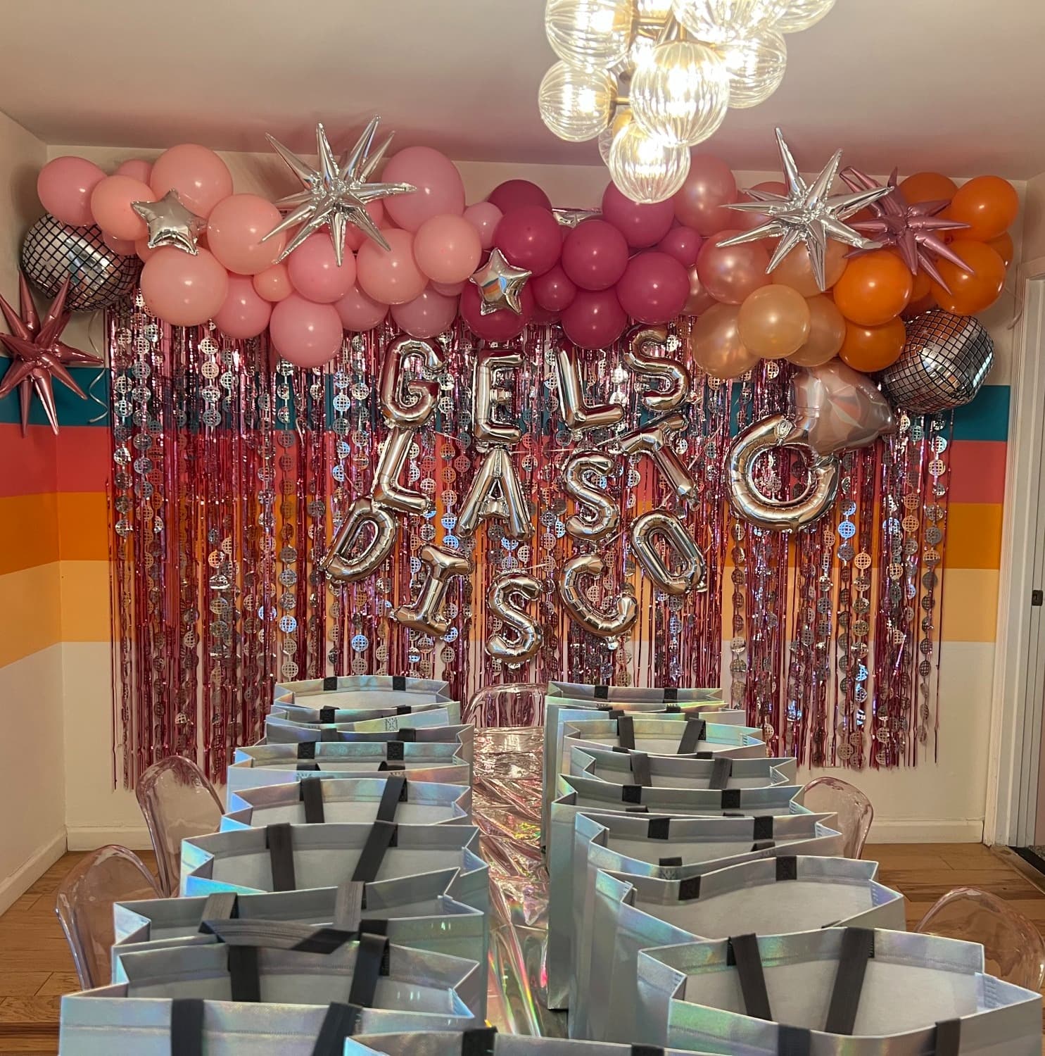 Bachelorette decor complete with gift bags lined up on a table, balloons, streamers and silver signage.