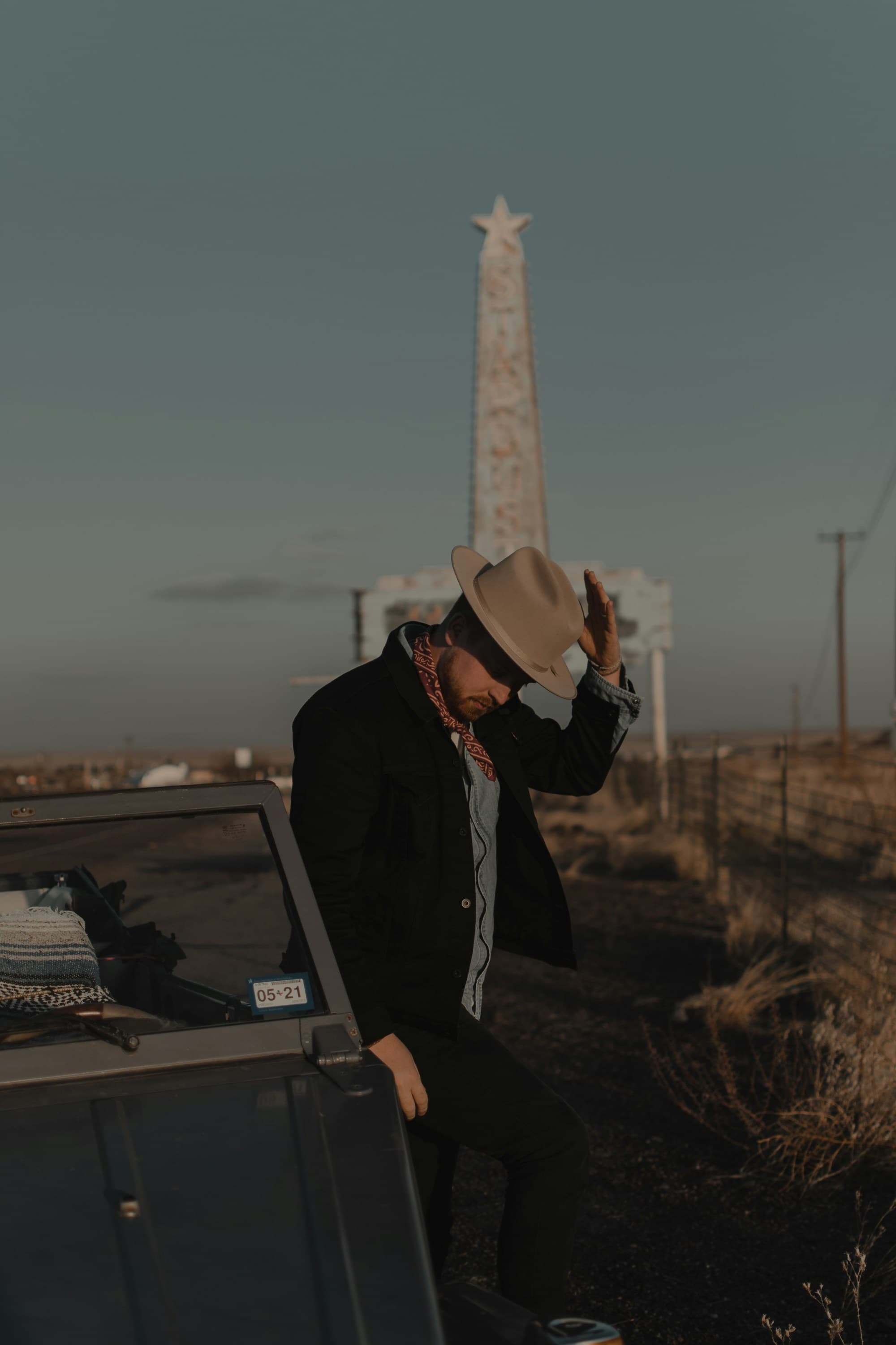 A picture of a man holding tipping a cowboy hat in front of a Texan monument.