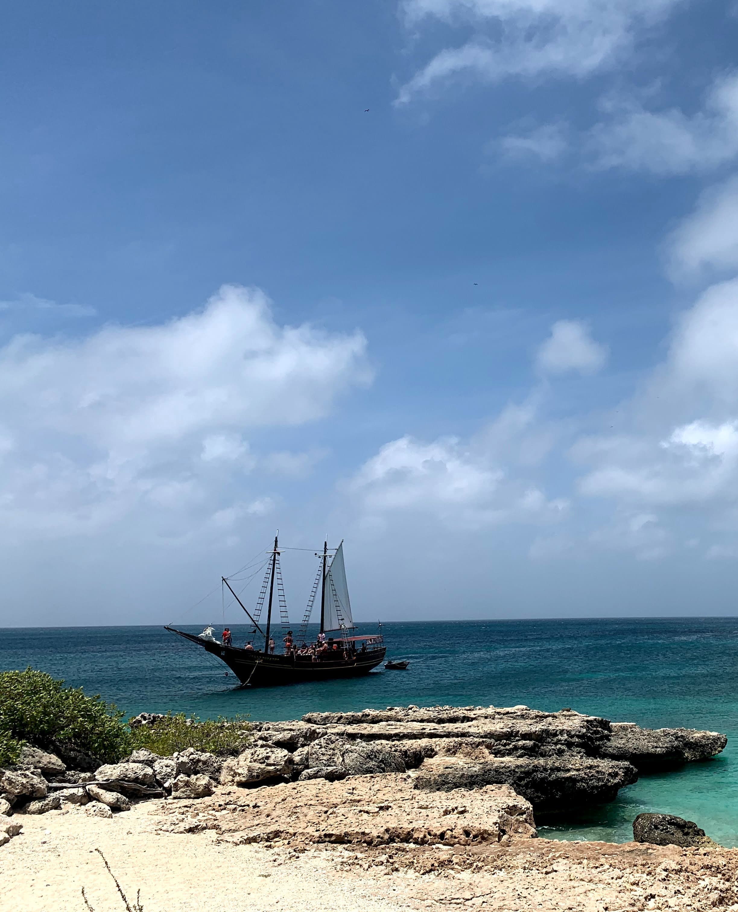 A coastline in Aruba with a ship in the distance on a sunny day.
