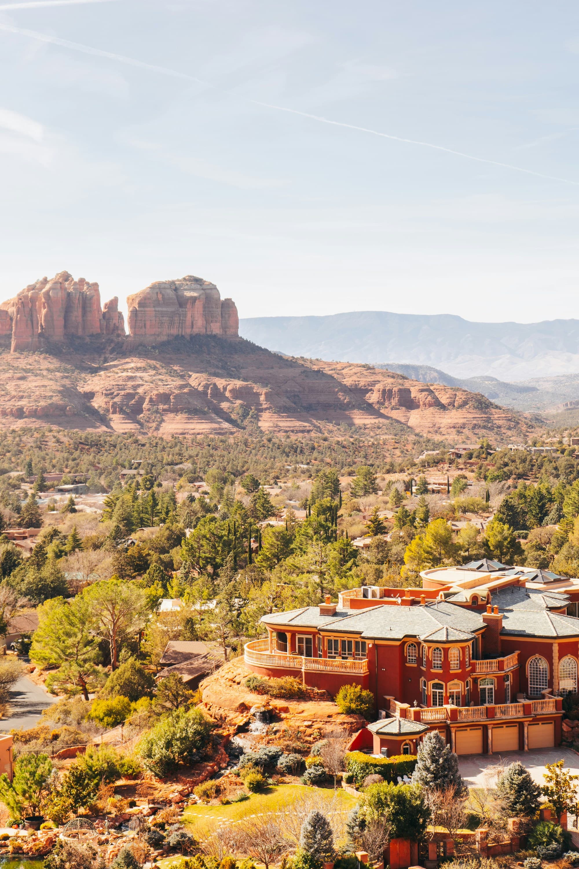 A view of red rock canyons, desert terrain and an elaborate red and orange toned building in the forefront.